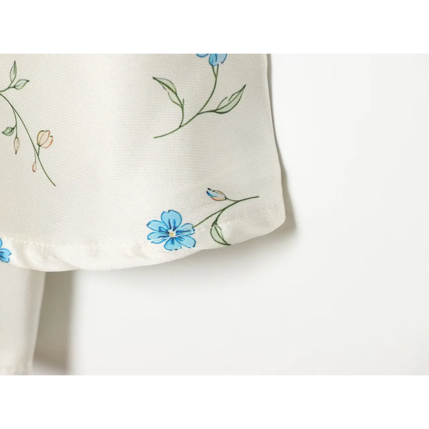 Close-up skirt hem stitching detail, silky white fabric with scattered blue floral pattern