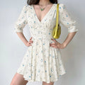 Woman model wearing white satin floral mini dress, deep V neck, puff elbow sleeves, corset waist, casual outfit studio shot
