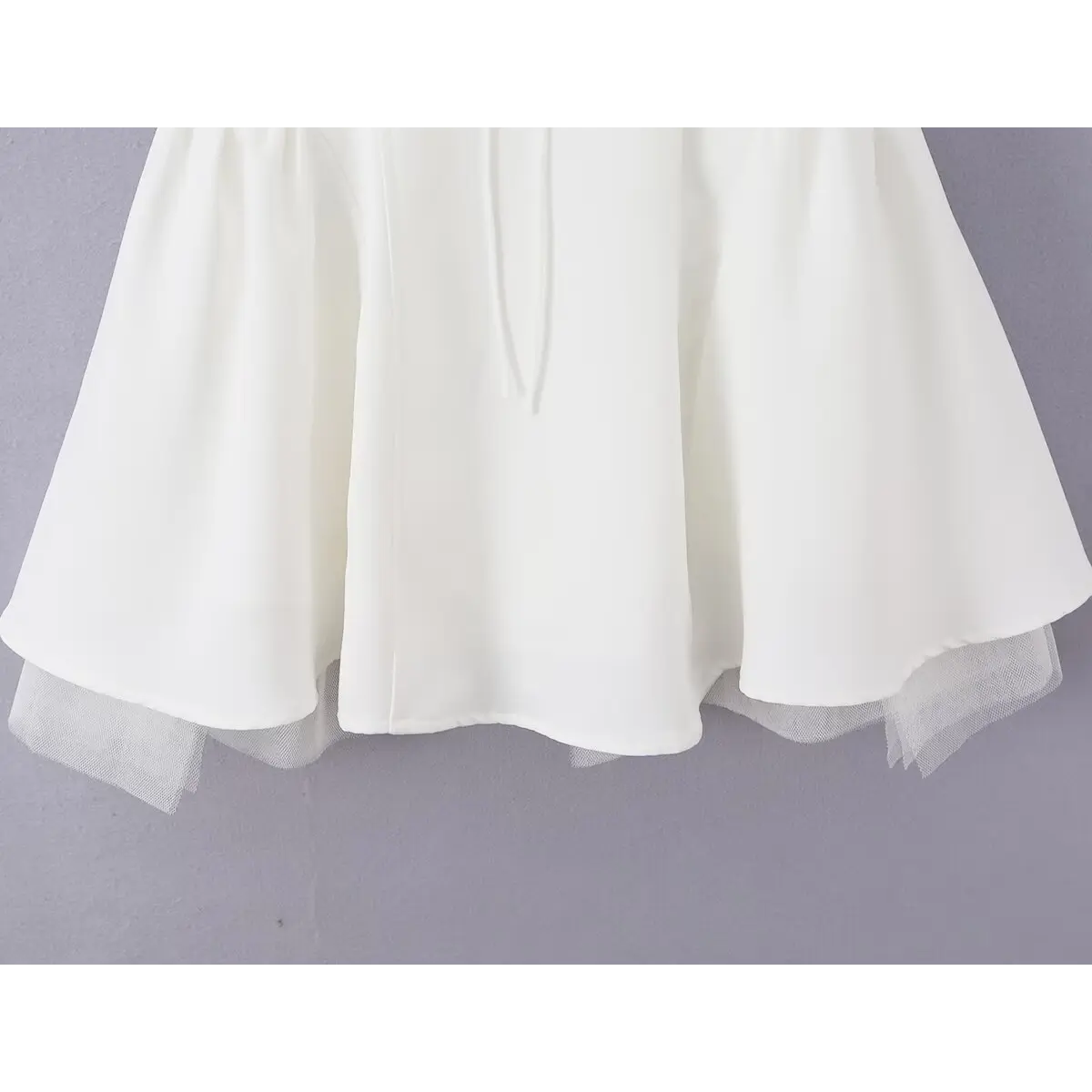 Close-up of the flared skirt hem and sheer tulle lining on the white bow dress