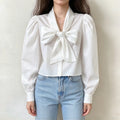 Model wearing white bow neck puff sleeve cropped blouse with jeans, front view