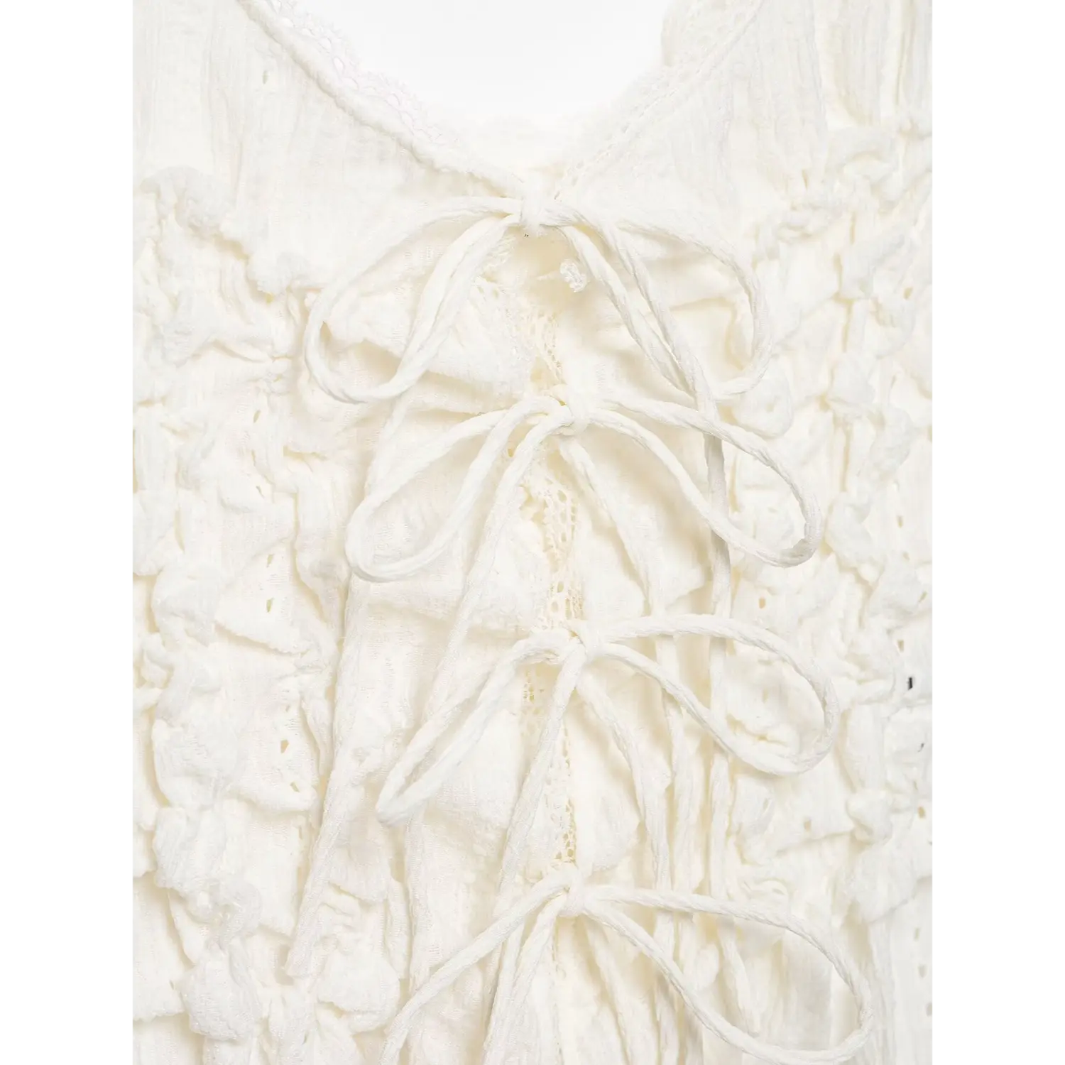 Macro close‑up of lace‑up tie knots on white cami top back, lace insert between fabric ties, crinkled texture fabric, white background