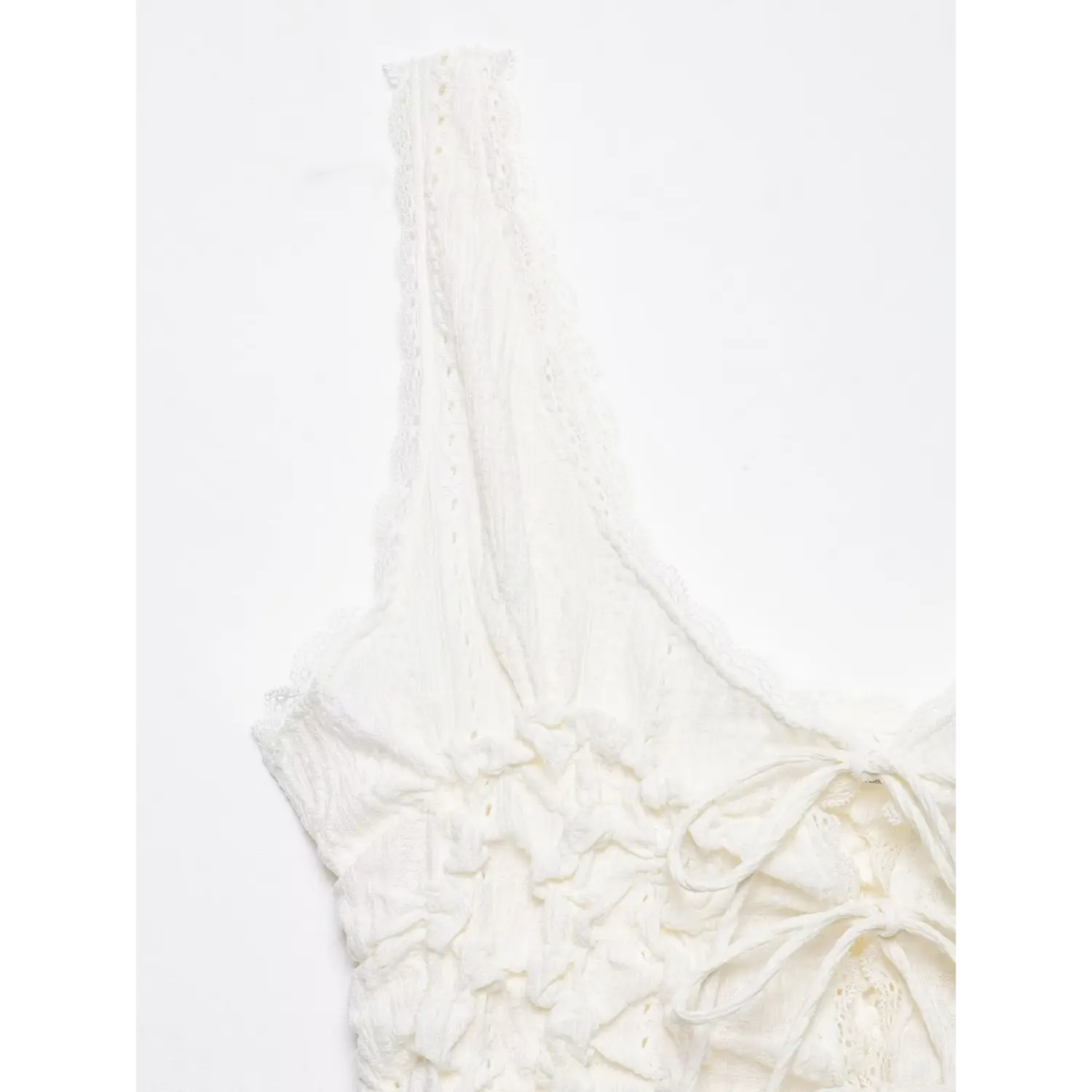 Close‑up shot of shoulder strap and v‑neckline, delicate scalloped lace trim on white crinkle camisole top, white background