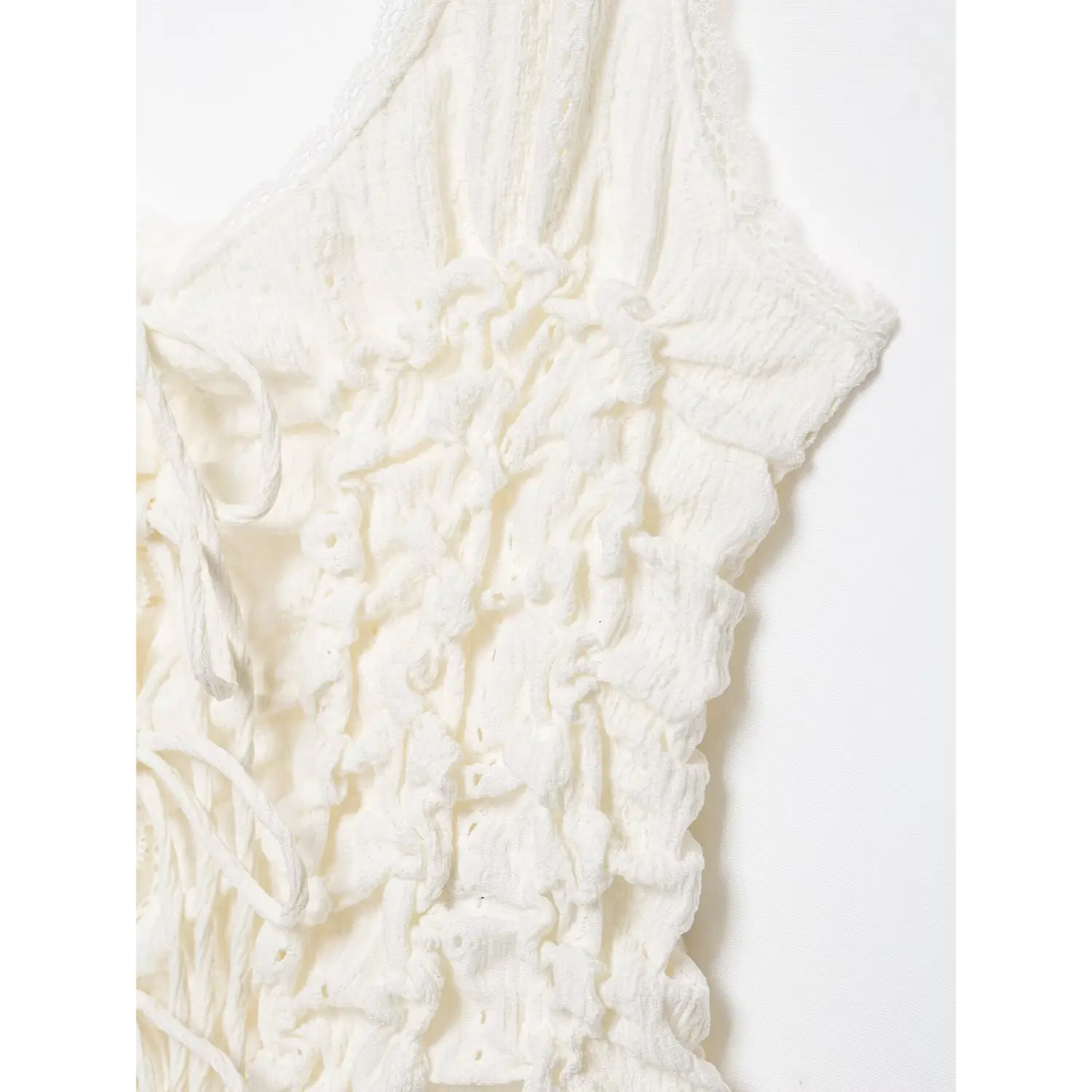 Close‑up side bodice detail of white cami top, heavily ruched crinkled eyelet fabric, scalloped lace trim, white background