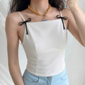 Lifestyle wearing shot of white camisole with black bow straps, paired with light blue denim jeans