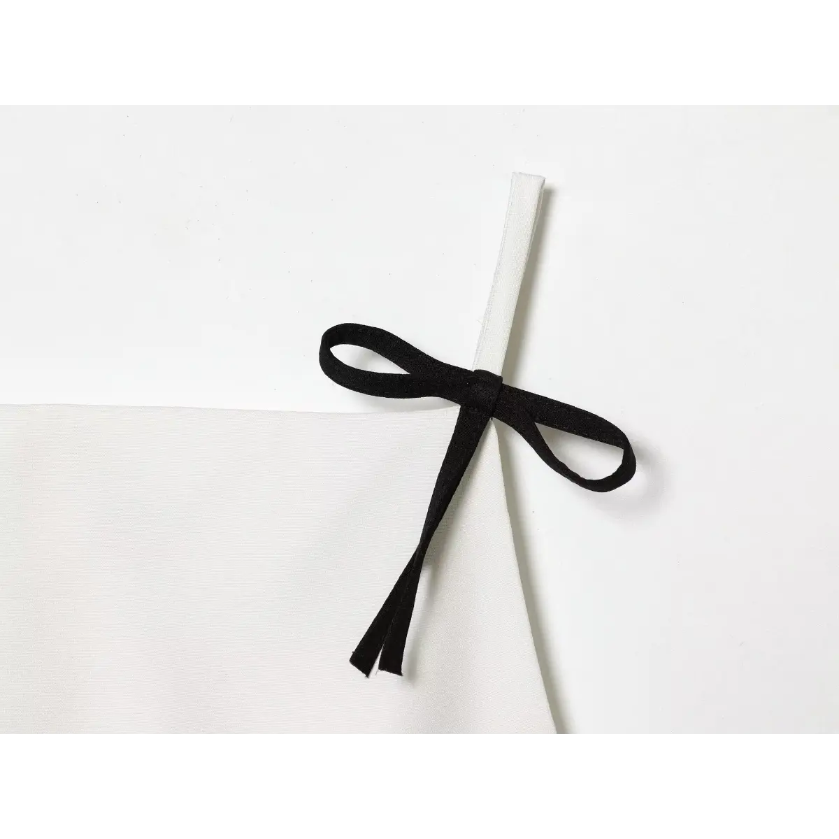 Close-up of the black bow tied to the thin white strap of the camisole