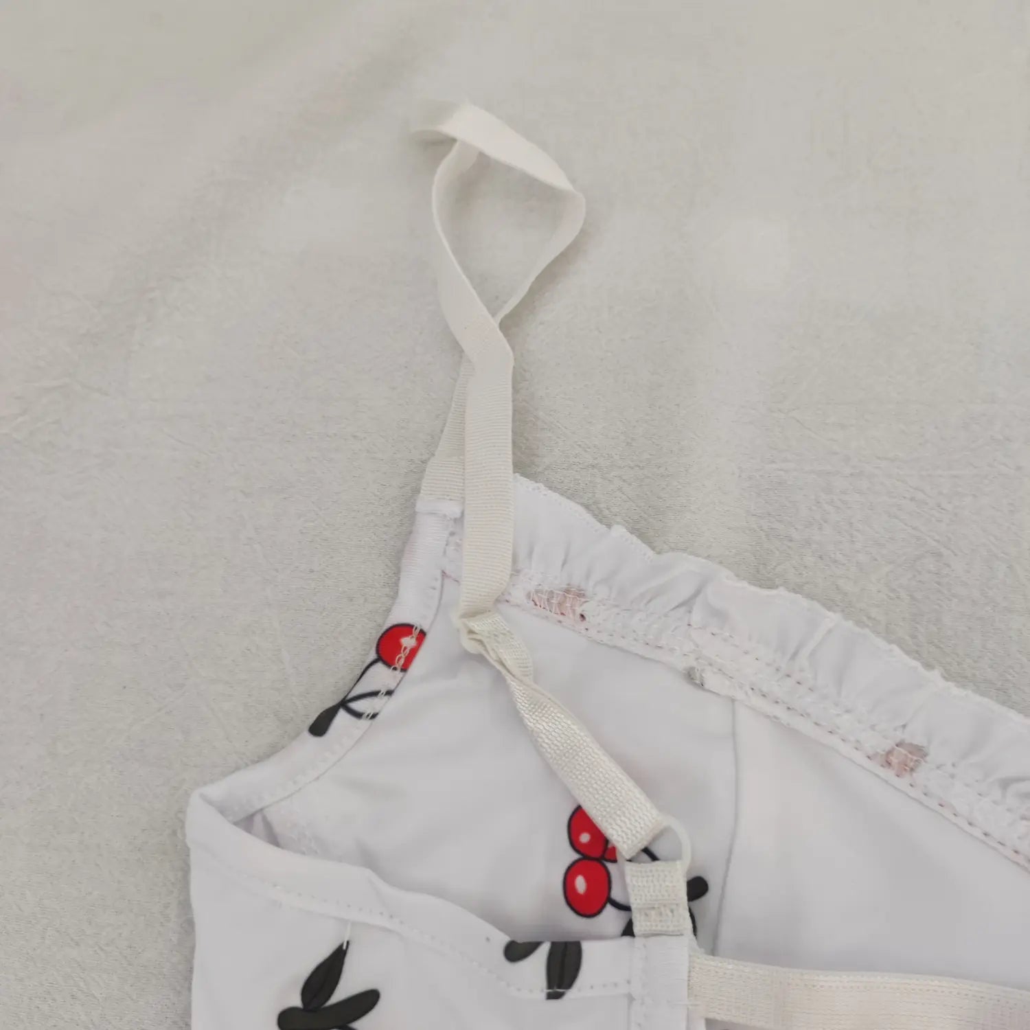 Close‑up inner view adjustable spaghetti strap and ruffle trim of white cherry print bodysuit