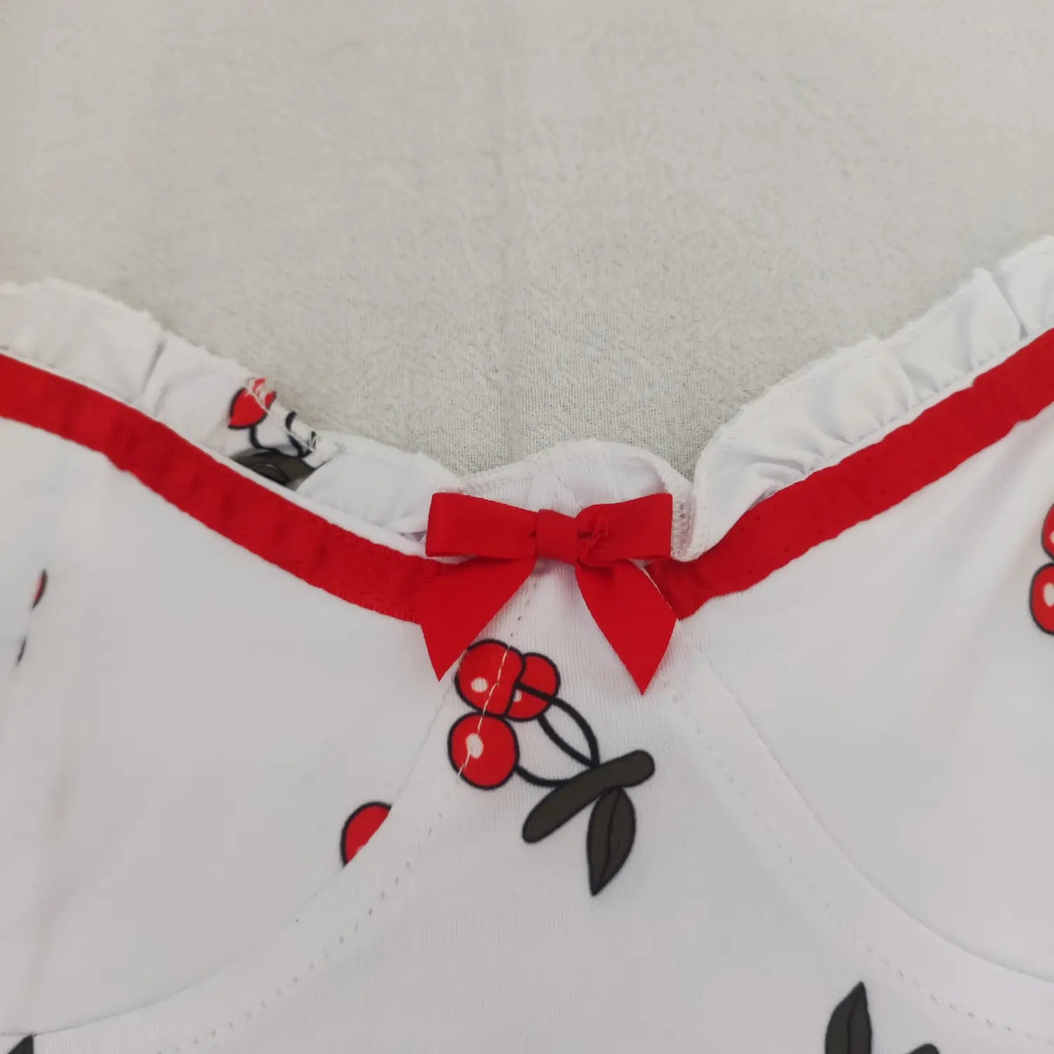 Flat lay full front view white cherry print bodysuit sweetheart neckline red bow and ruffle trim
