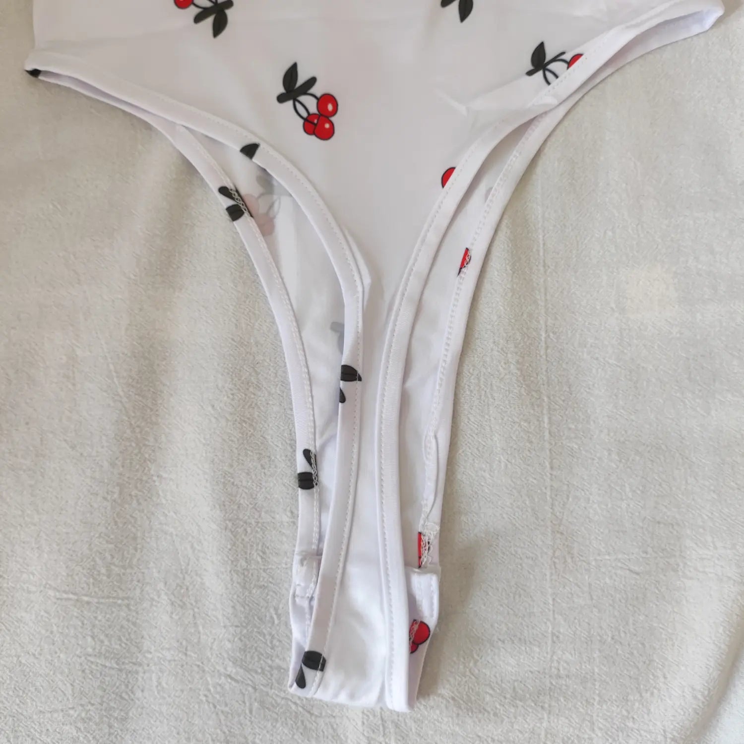 Close‑up high‑cut leg opening and seam finishing white cherry print bodysuit