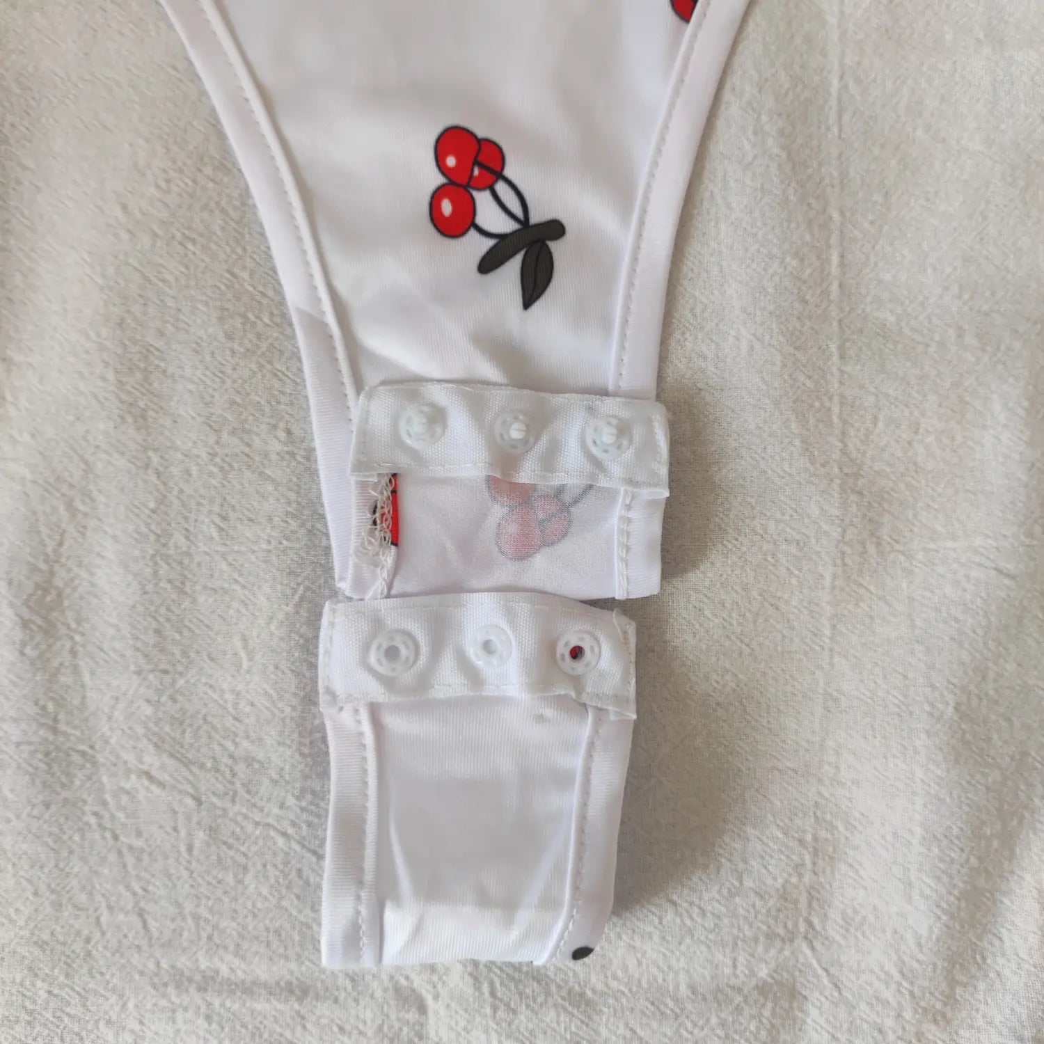 Close‑up multi‑position snap button crotch closure white cherry print bodysuit
