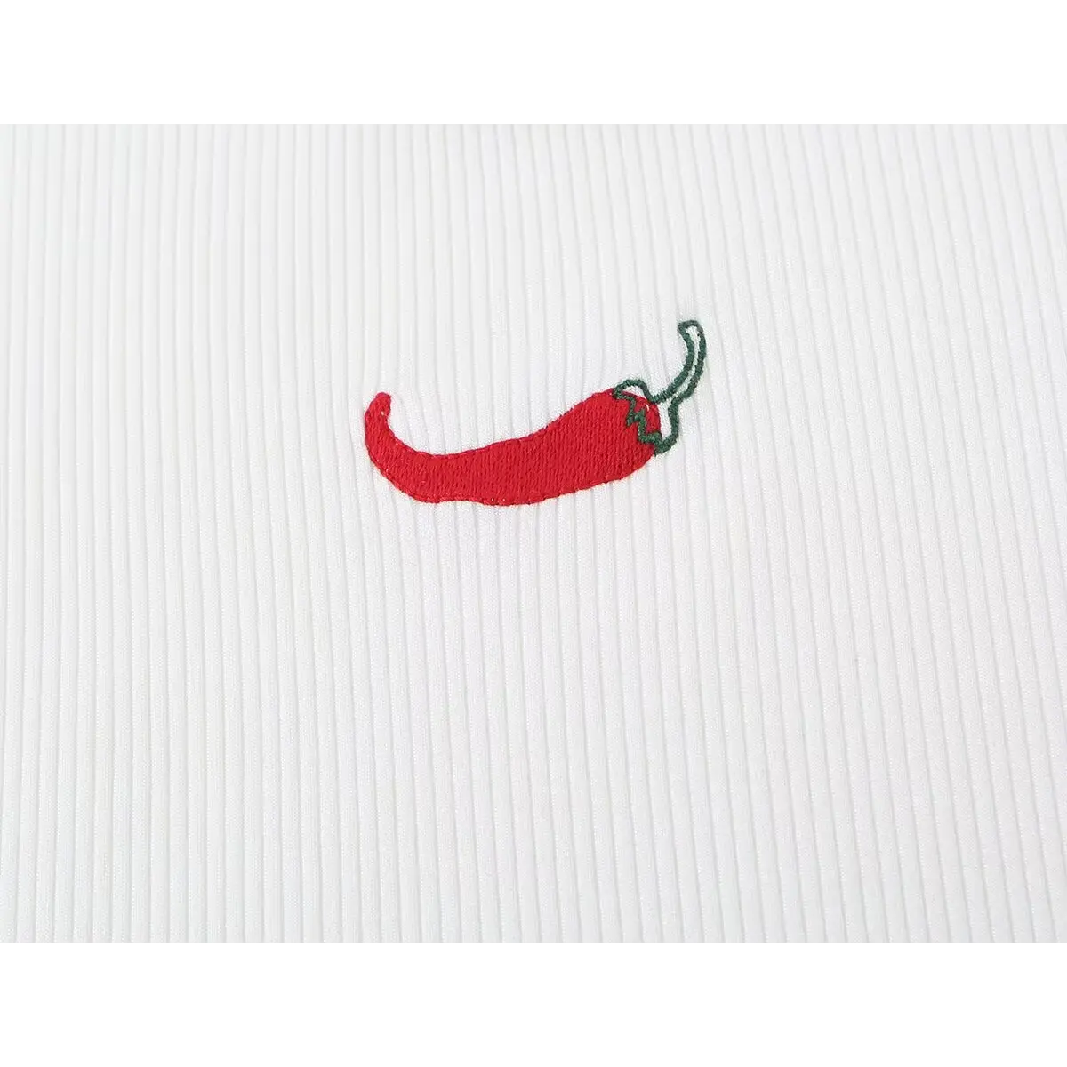 Close-up of the red chili pepper embroidery on the white ribbed tank top