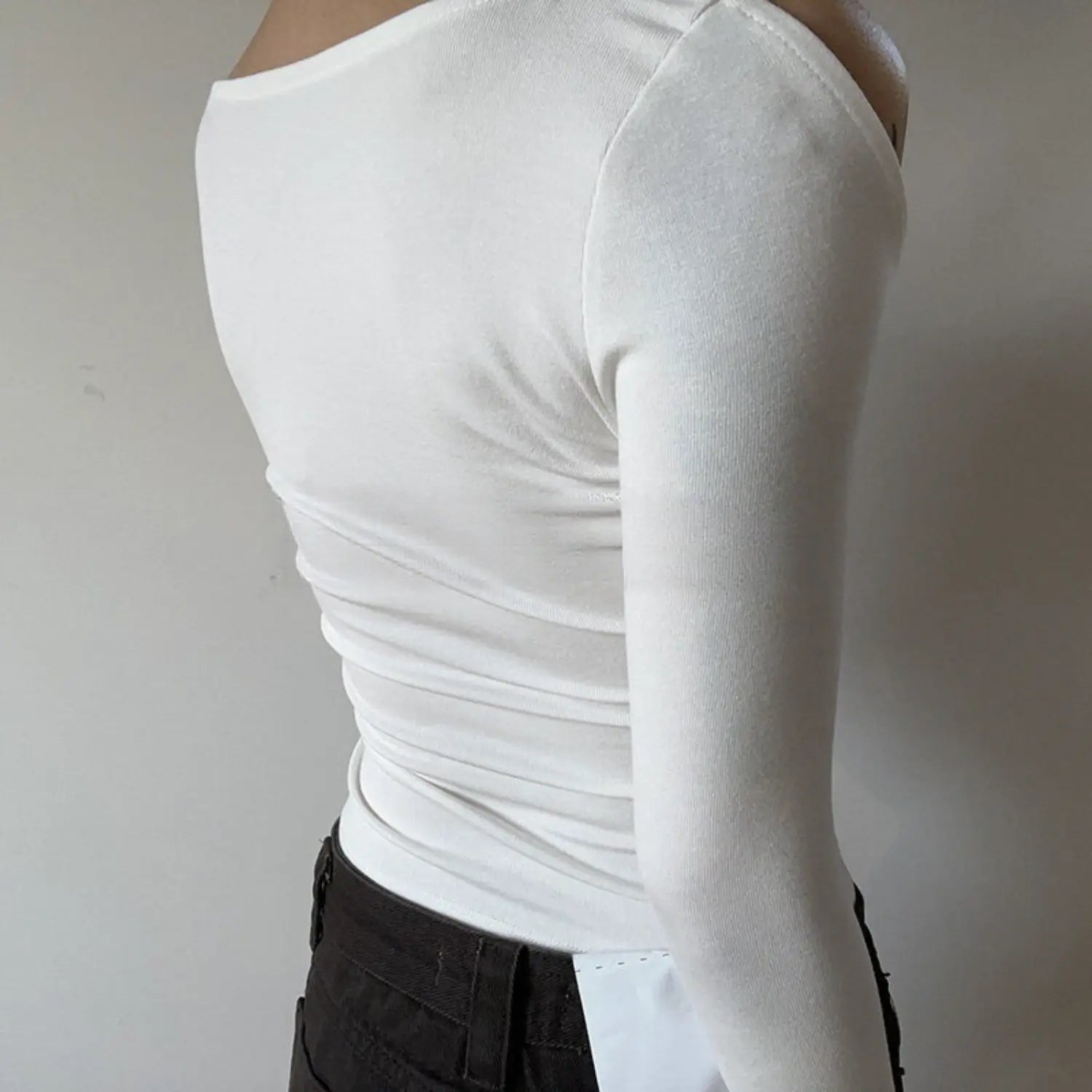 White spaghetti strap cold shoulder long sleeve top full back model shot, solid knit plain back ruched cropped fit, matched with dark denim minimalist casual outfit display