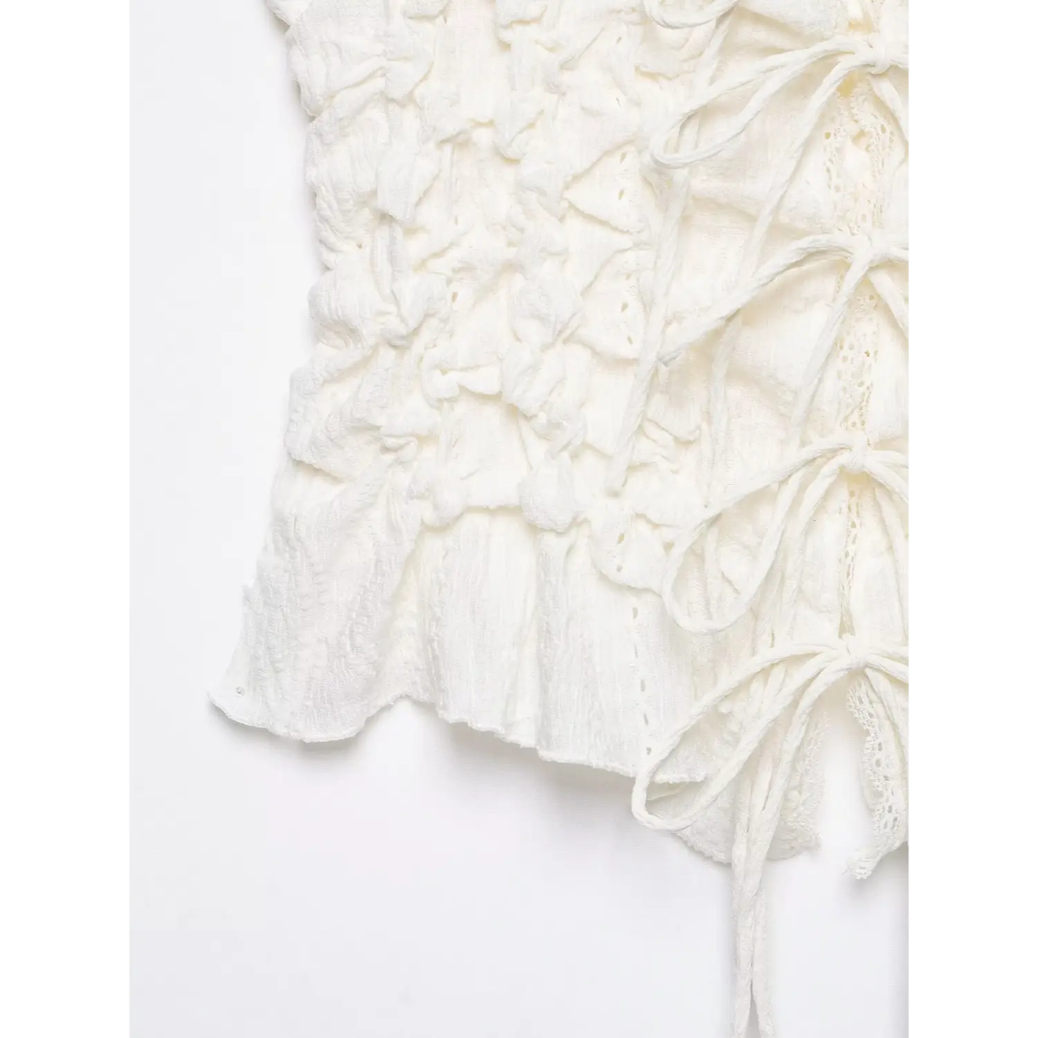 Close‑up side hem view of white cami top, ruffled peplum hem, ruched crinkle fabric texture, white background