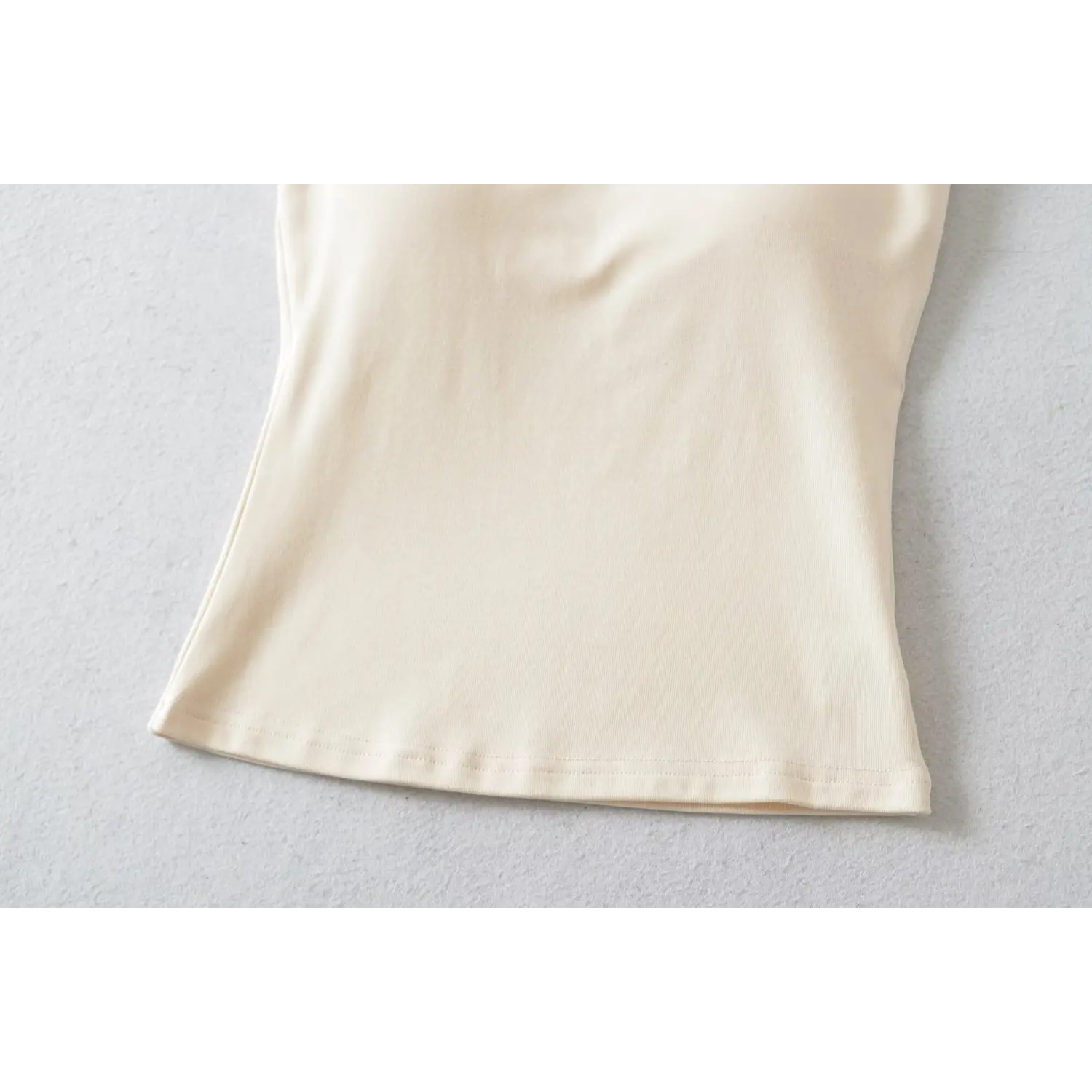 Close-up shot of hem for beige cami tank top with black piping trim