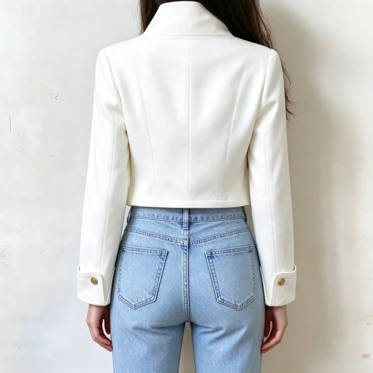 Female model back view, white cropped tailored jacket, vertical seam detailing on back, long sleeves with gold cuff buttons