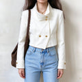 Female model wears white cropped stand collar jacket, asymmetric double breasted gold buttons, long sleeves with gold cuff buttons, front torso shot