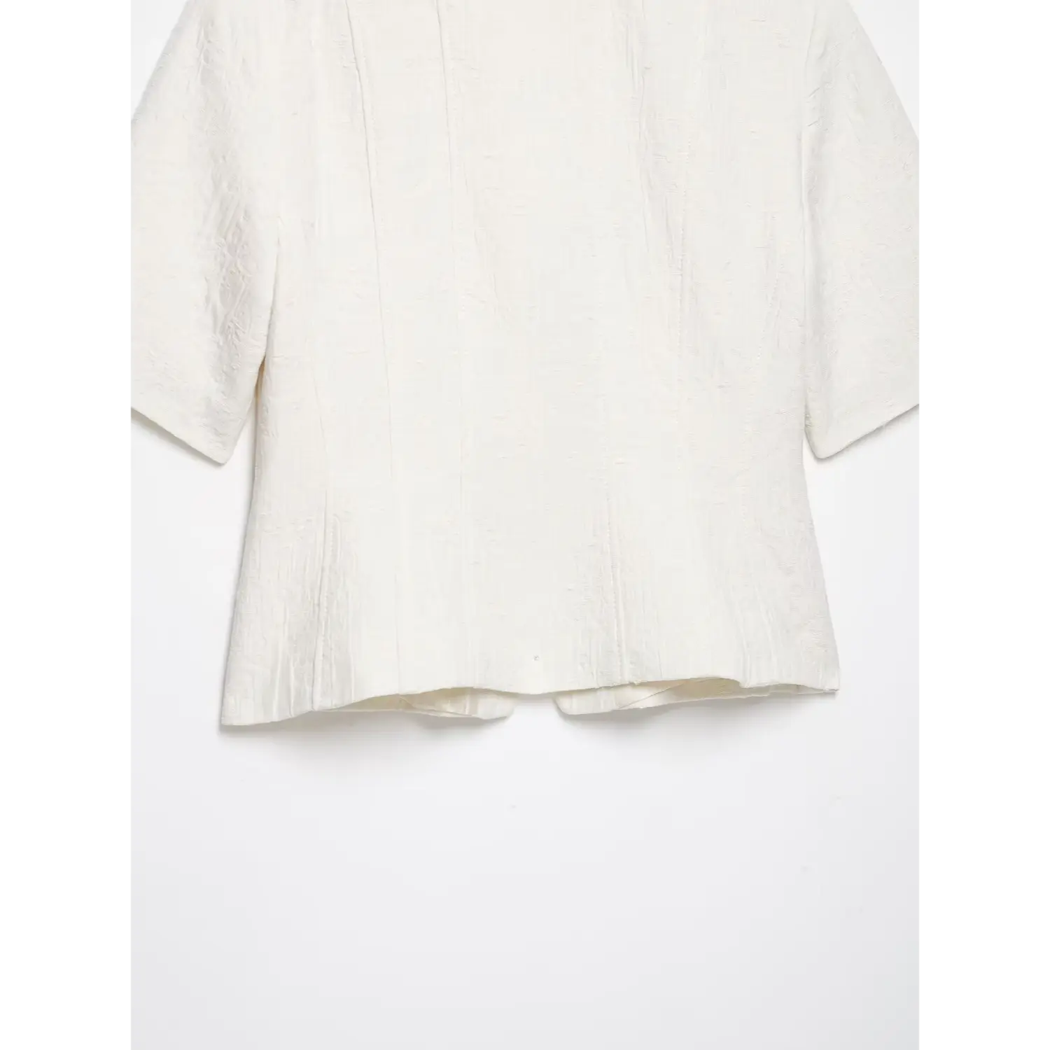 Partial back flat‑lay shot of white textured cropped short sleeve jacket, showcasing back tailored seams and finished bottom hem, white background