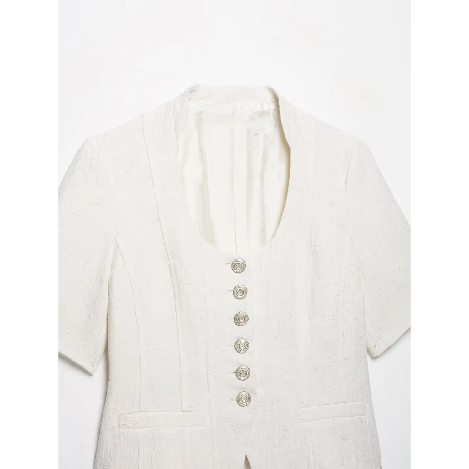 Close‑up front view of white cropped short sleeve jacket, showcasing u‑neckline and full vertical silver spiral button placket, patch pockets, white background