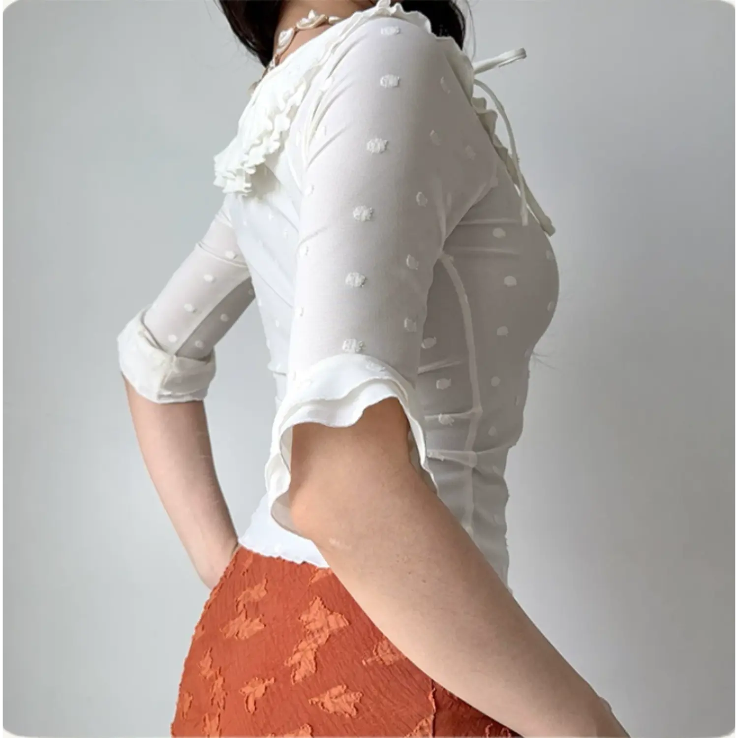 Back lifestyle shot on model of white textured dot mesh blouse, layered ruffle neckline, adjustable side tie, mid flared cuff sleeves