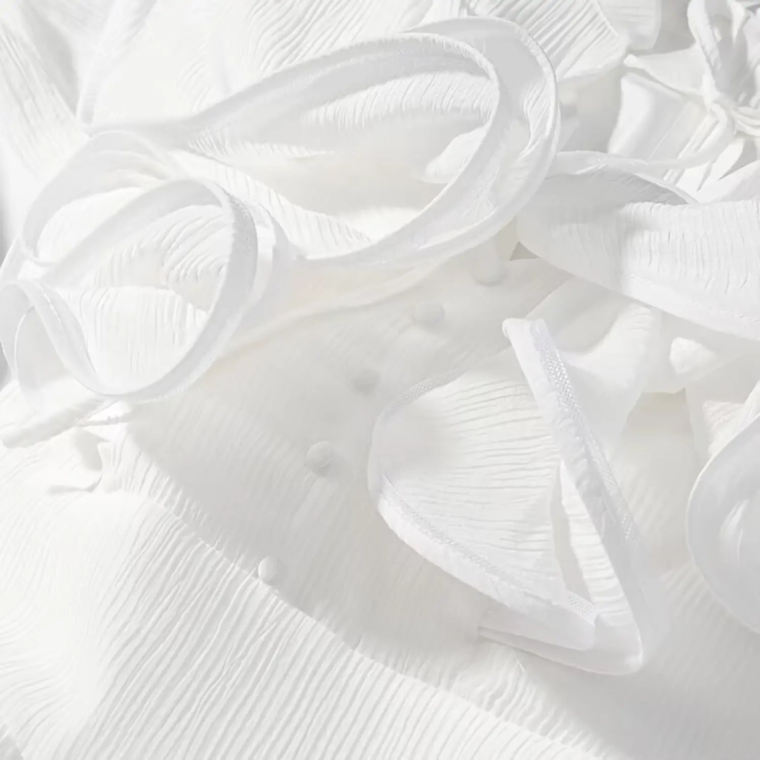 Close-up view of 3D spiral flower decoration, ruffle and covered buttons on white wrinkled fabric dress