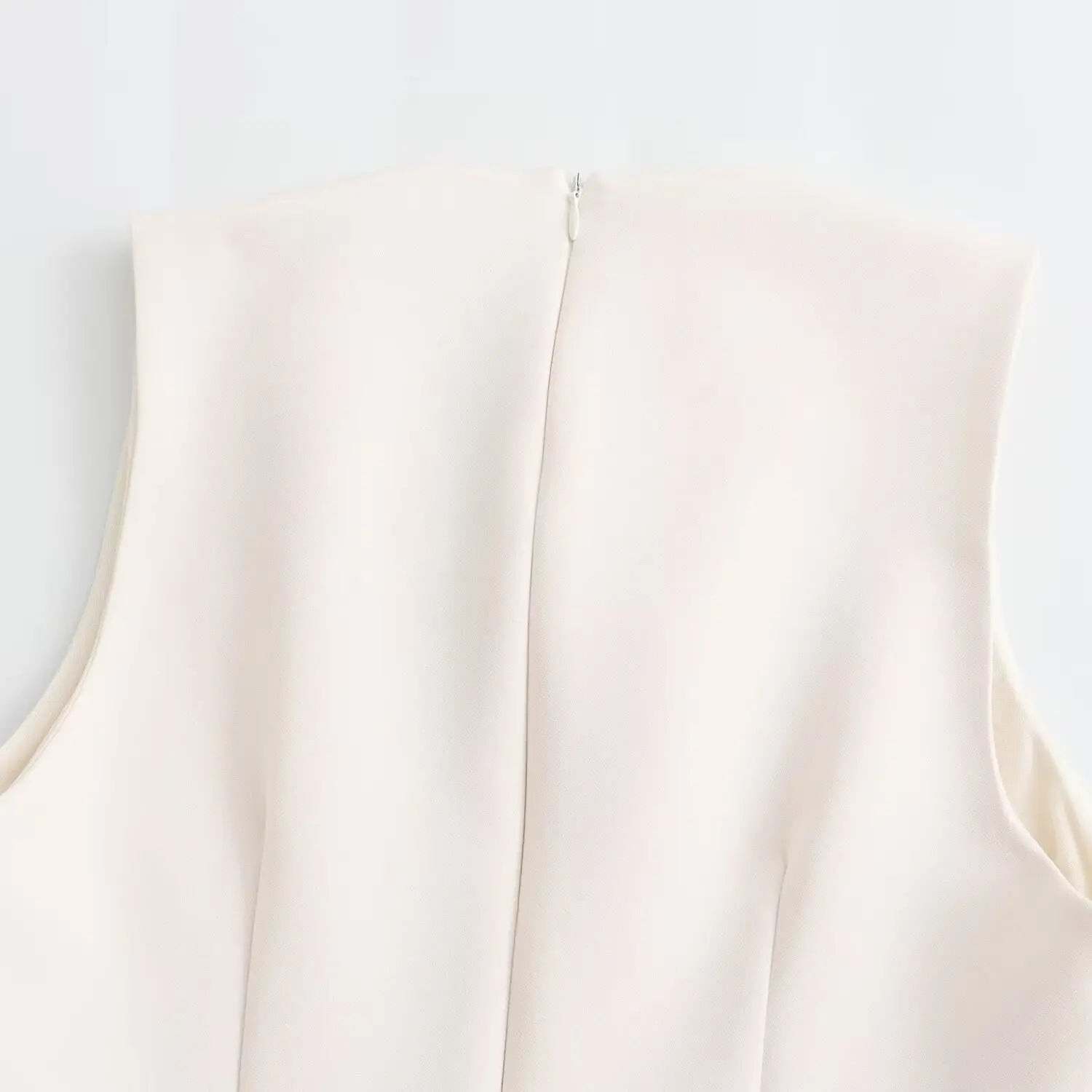 Close‑up top of center‑back invisible zipper on white sleeveless mini dress, tailored back panel
