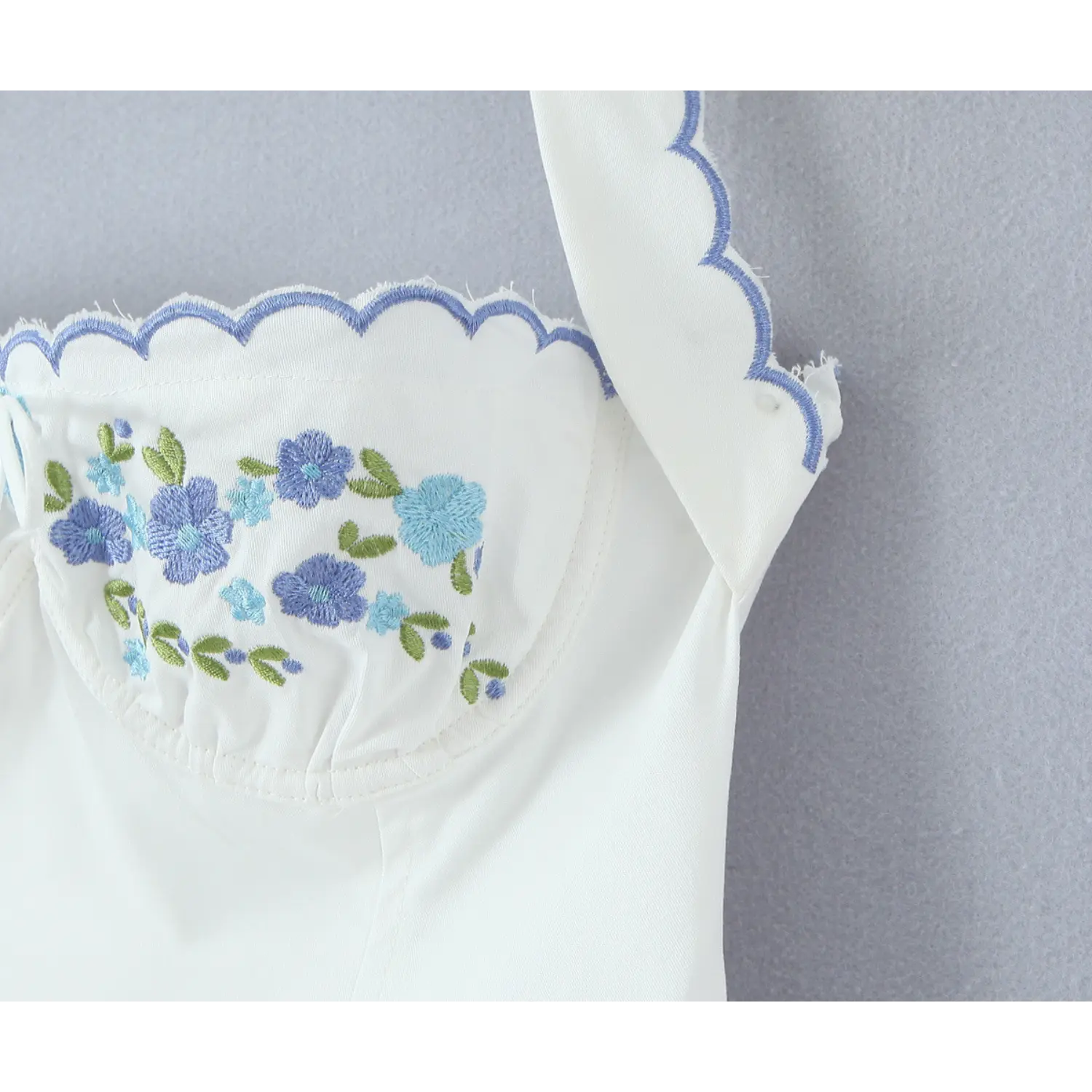Extreme closeup of floral embroidery, blue flower stitch detail on white halter dress bust scalloped trim