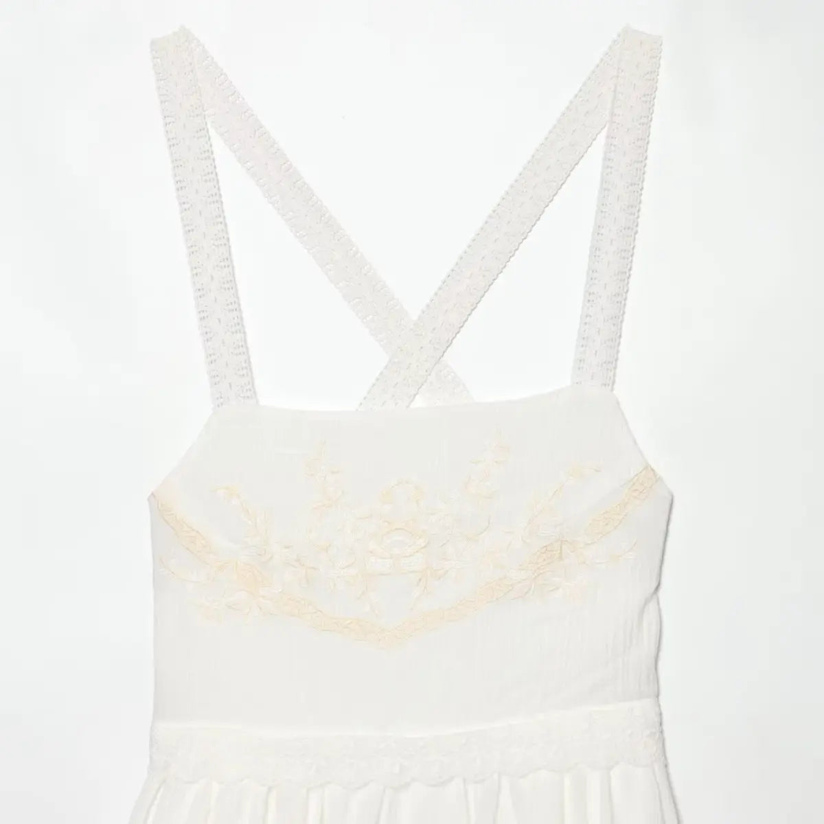 Upper view of white dress with crisscross lace straps, highlighting square neckline and chest embroidery.