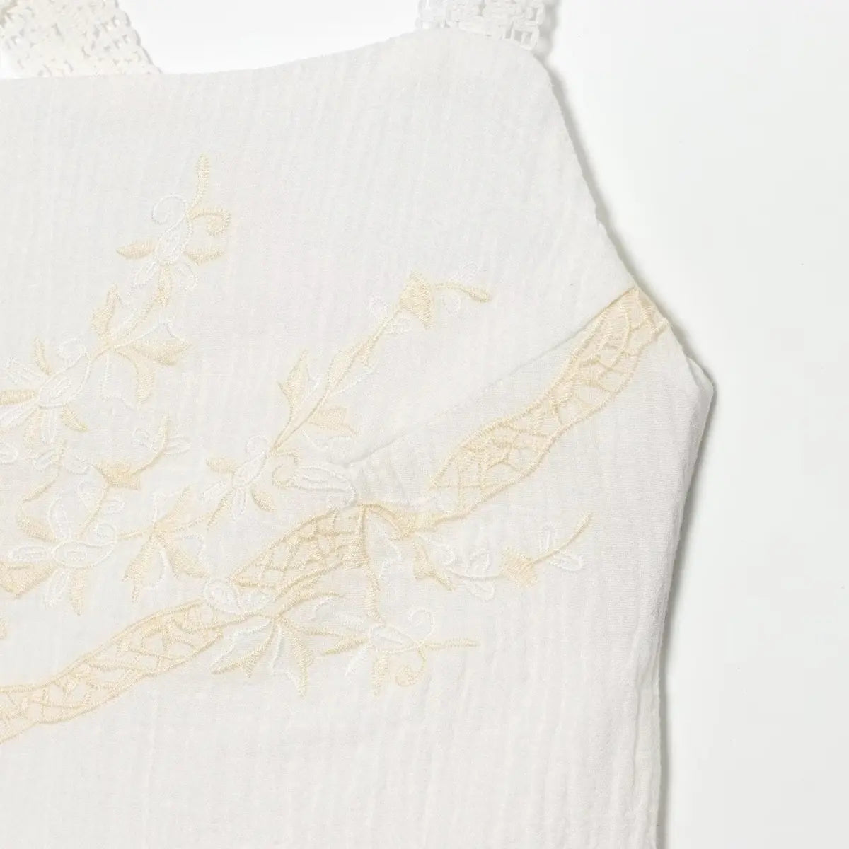 Close-up of the floral embroidery on white dress, showing delicate beige threadwork and textured fabric.