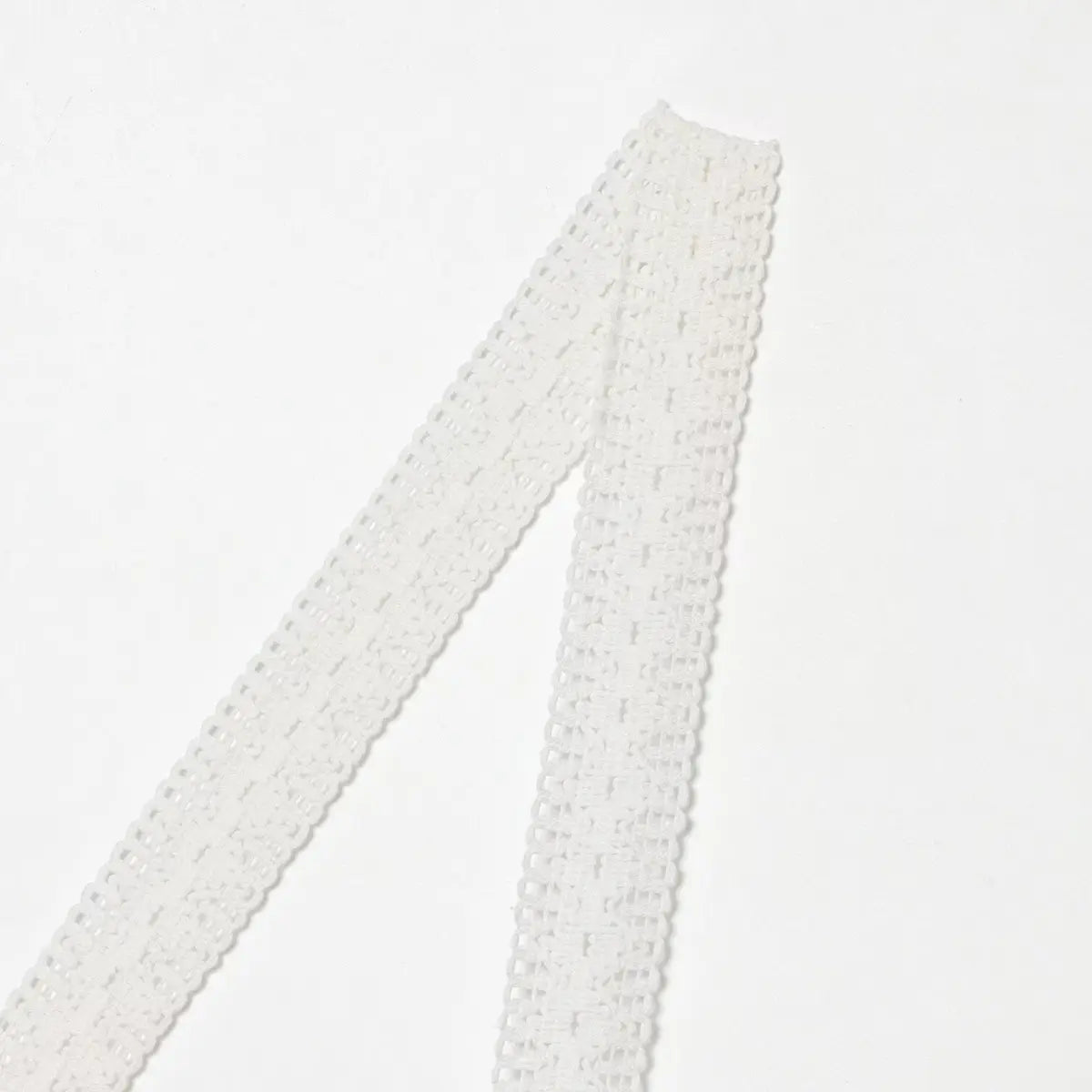 Close-up of the lace strap on white dress, showing openwork texture and woven pattern design.