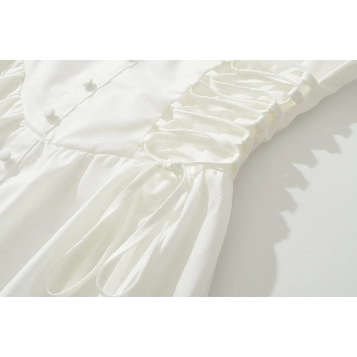 Detail shot of adjustable side lace-up ties and corset waist construction of white sleeveless mini dress