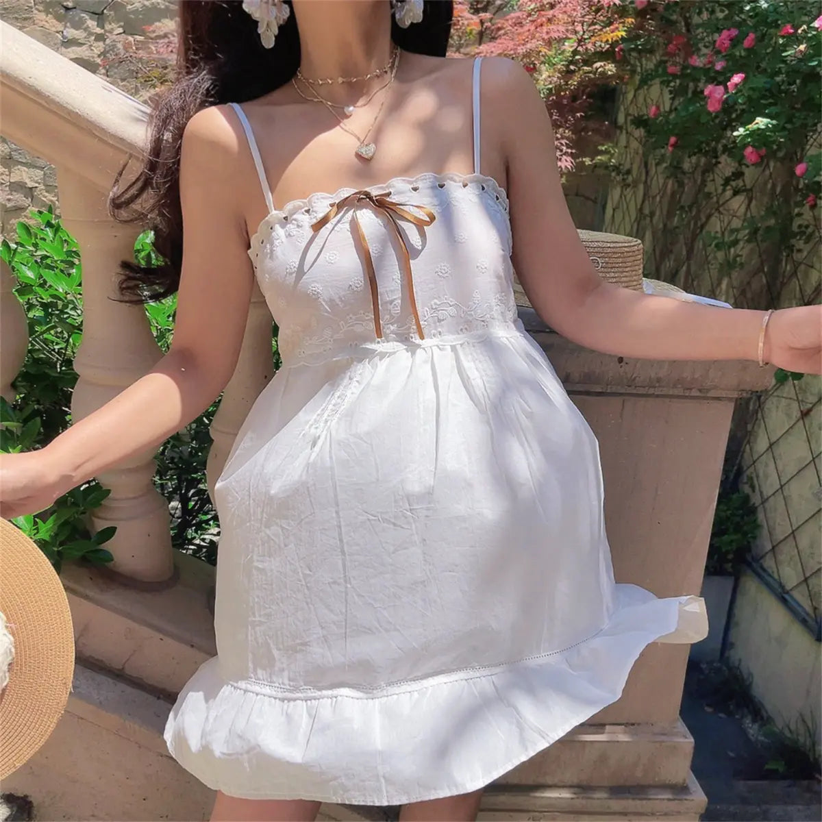 Close-up shot of a model wearing a white embroidered cami dress, highlighting the lace-trimmed neckline and brown ribbon bow.