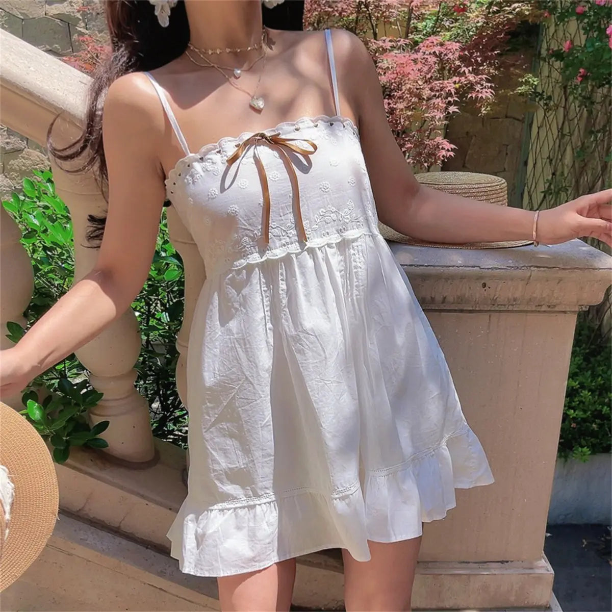 Full front view of a model in a white embroidered cami dress, showing the floral embroidery, gathered skirt, and ruffled hem.