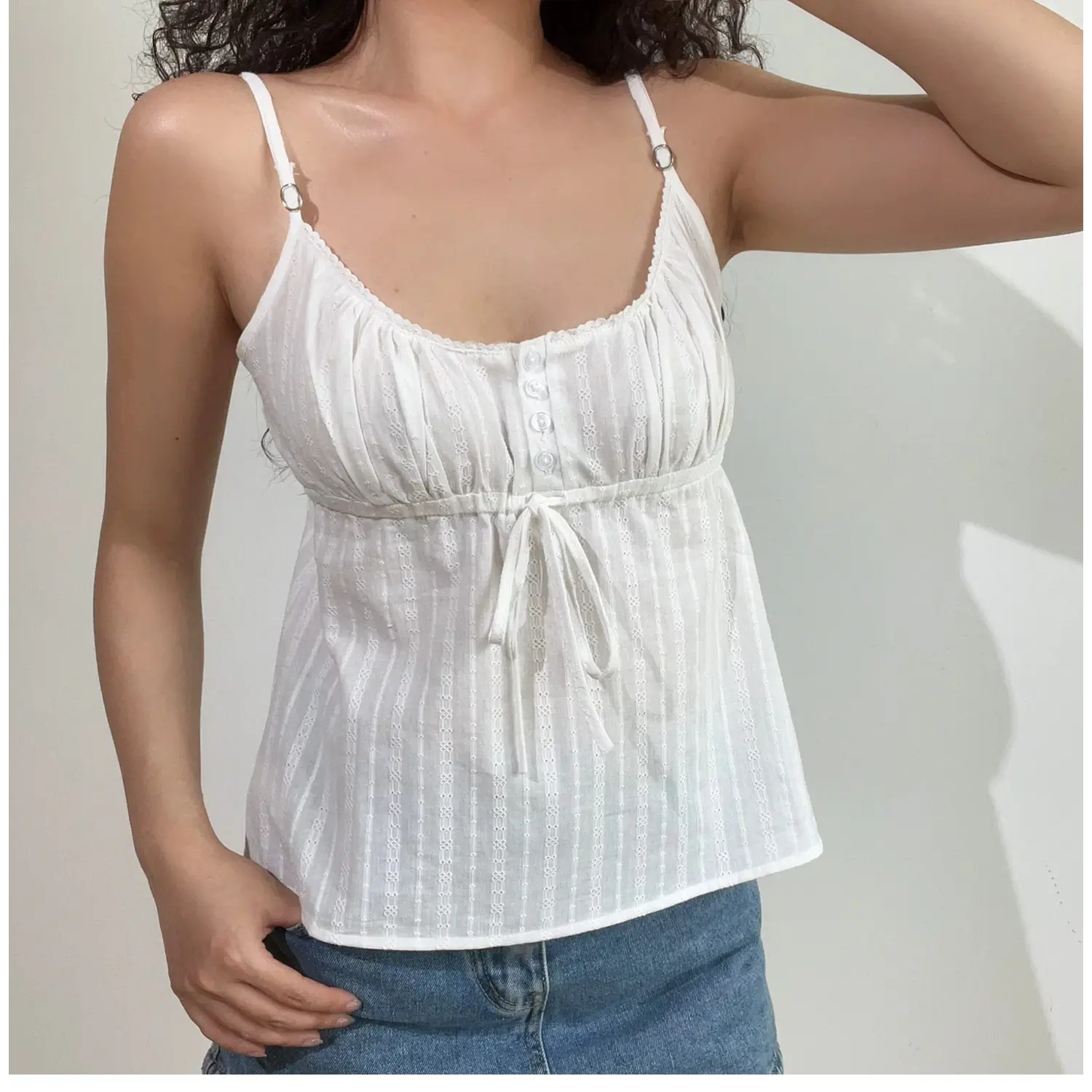 Close-up lifestyle shot of model in white textured cami top with adjustable straps