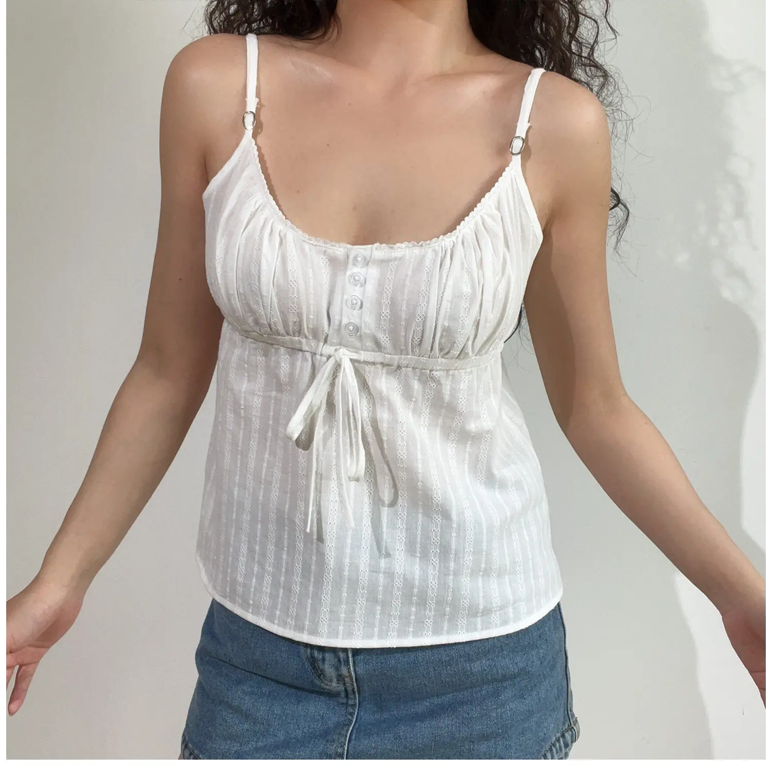 Lifestyle shot of model wearing white textured cami top with buttons and drawstring detail