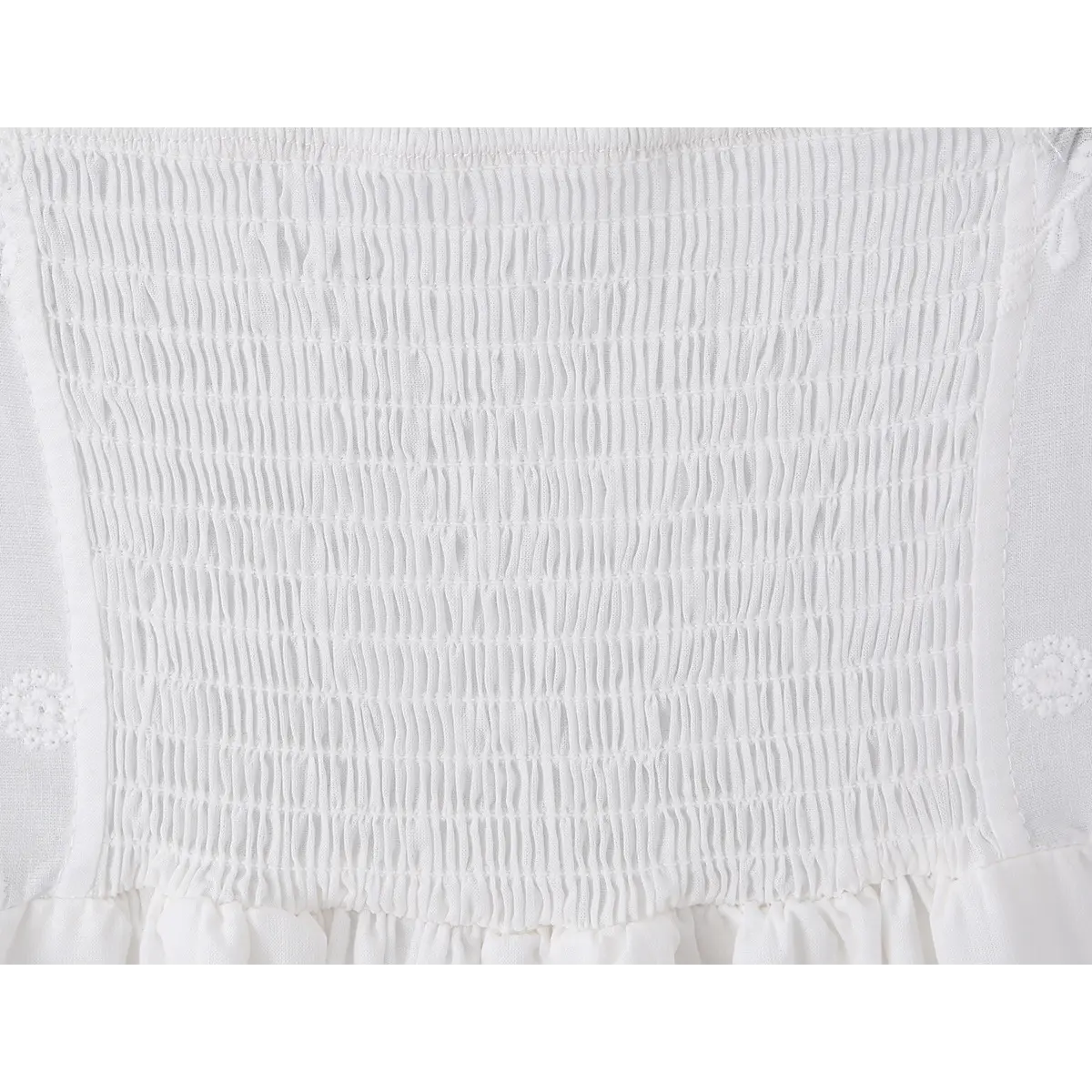  Close-up detail shot of the smocked elasticated back panel on a white embroidered cami mini dress.