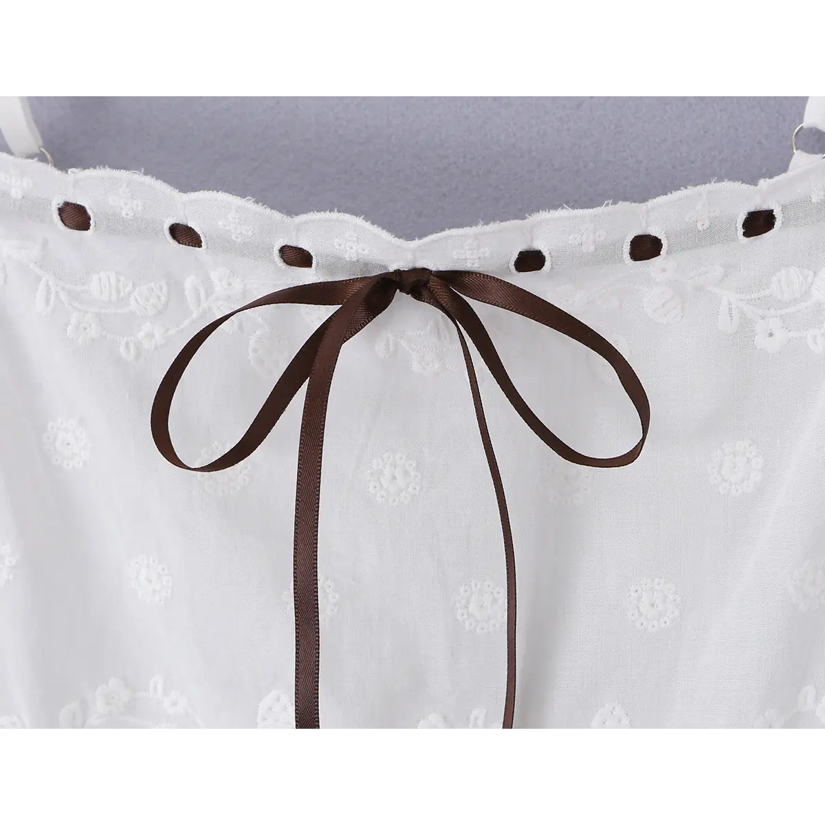 Close-up detail shot of the brown ribbon bow and eyelet neckline on a white embroidered cami mini dress.