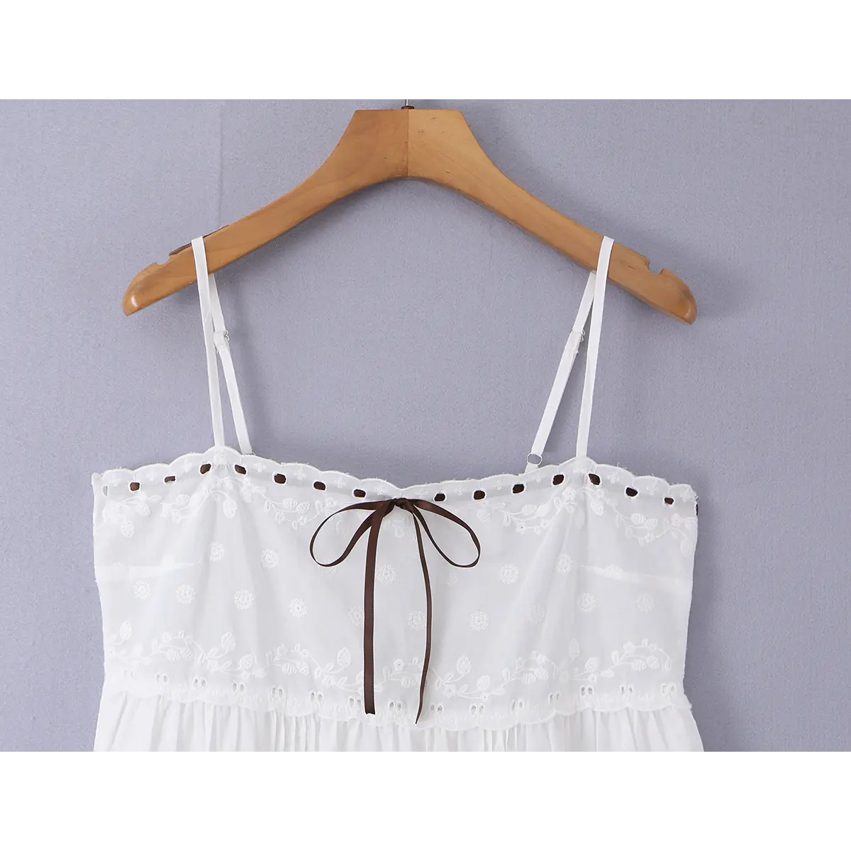 Close-up view of the adjustable spaghetti straps and embroidered neckline on a white cami mini dress.