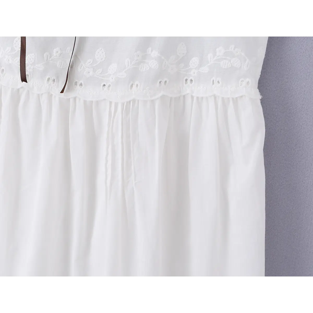 Close-up detail shot of the floral embroidery and scalloped trim at the waist of a white cami mini dress.