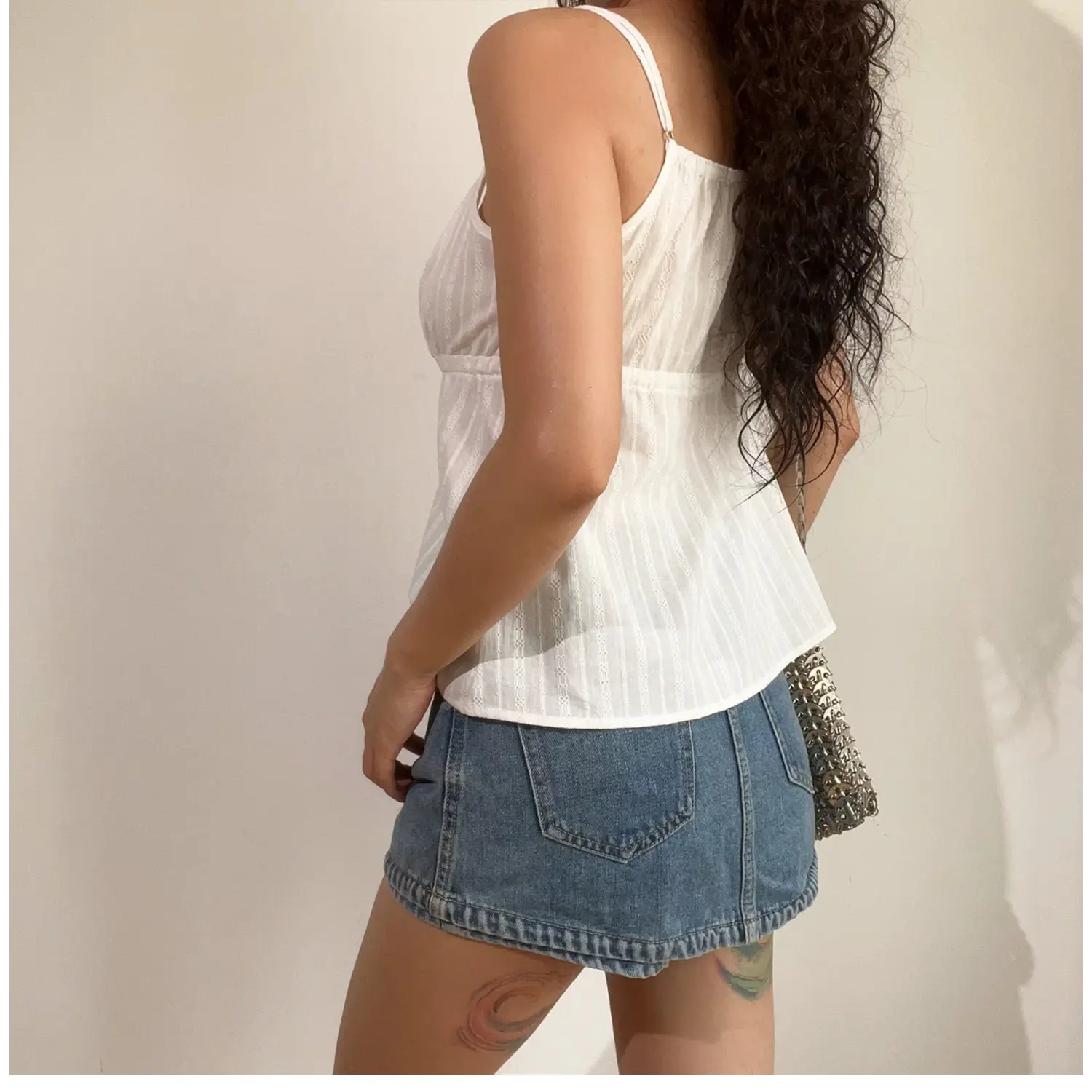 Profile shot of model in white textured cami top with denim shorts