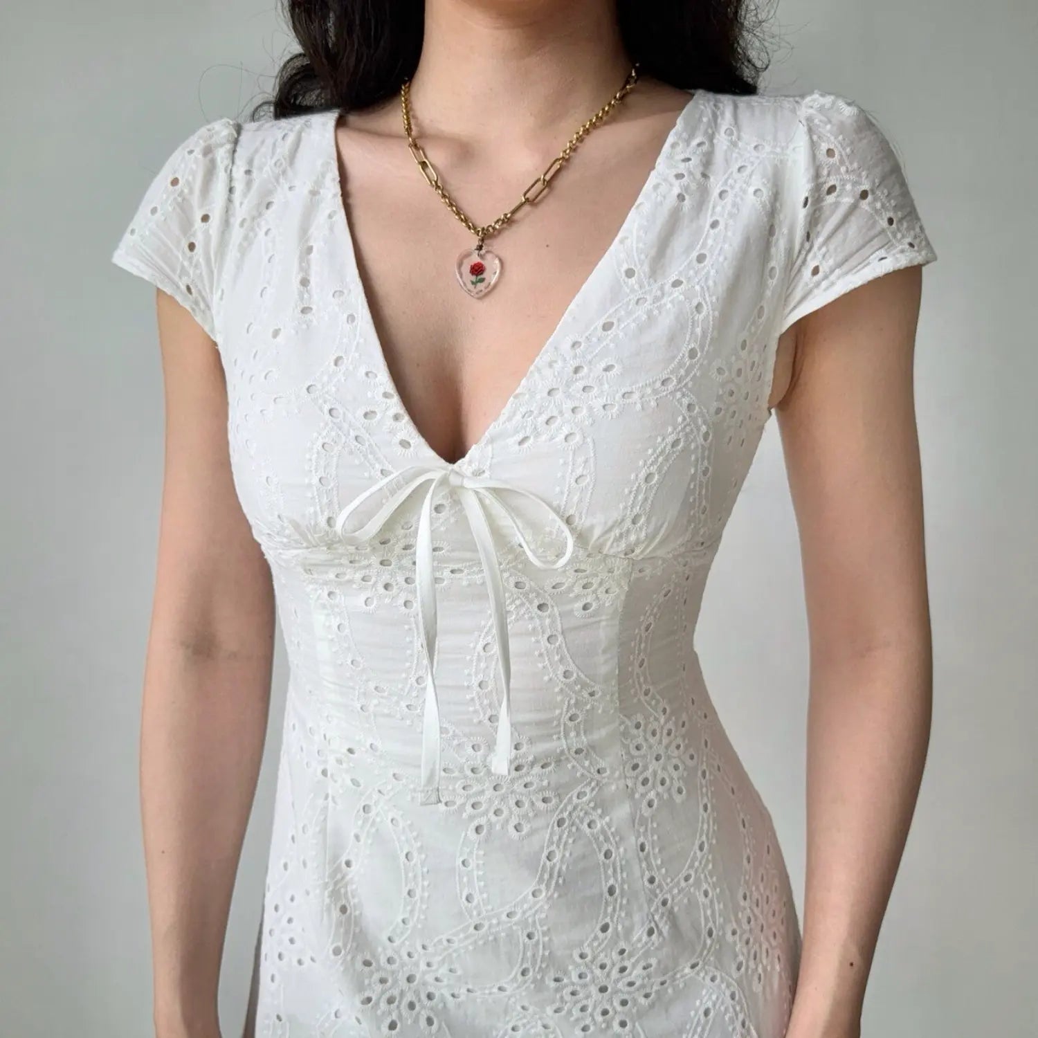 Close-up shot of the V-neckline and bow tie detail on a white eyelet embroidered mini dress
