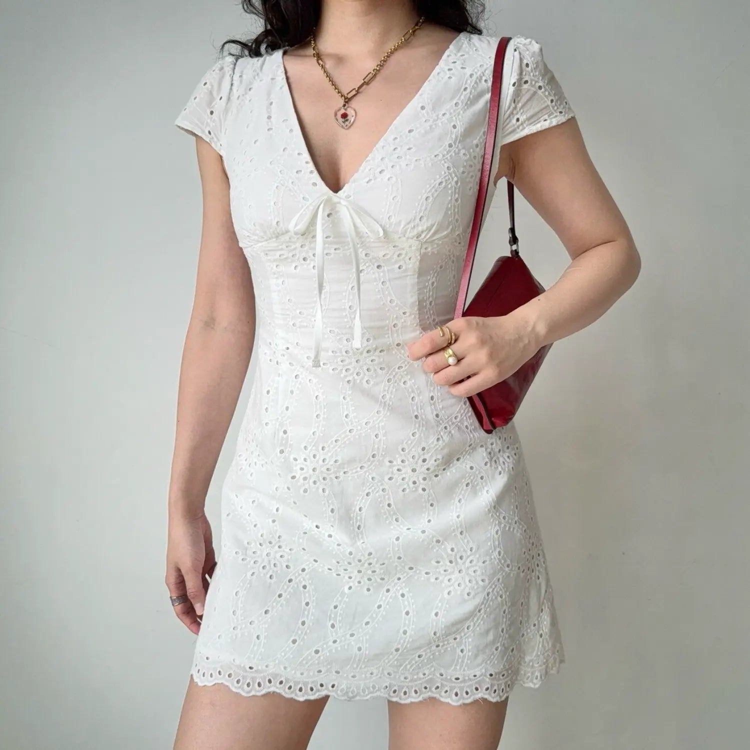 Full-body shot of a woman in a white eyelet embroidered mini dress, paired with a red handbag