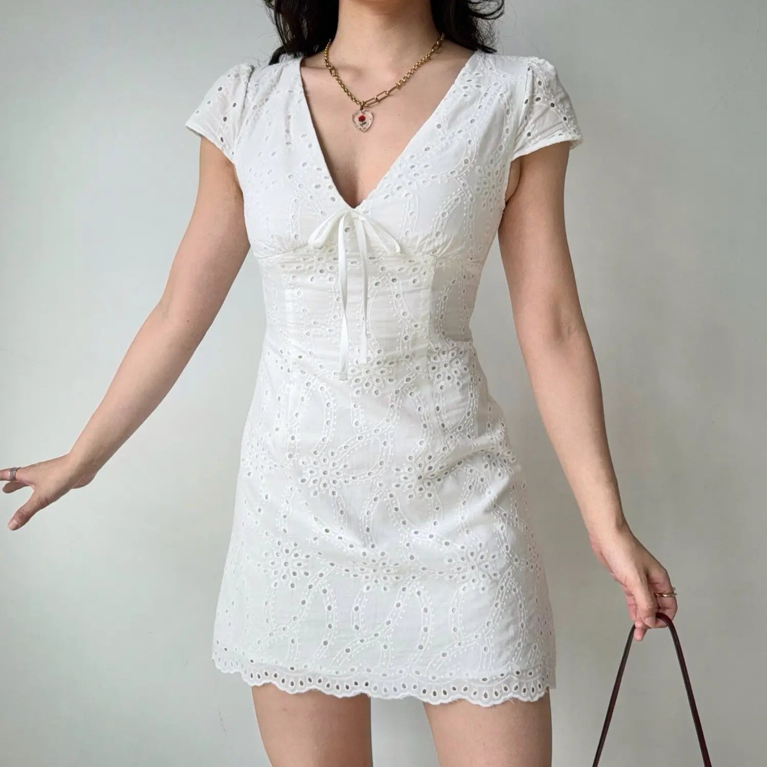 Full-body shot of a woman in a white eyelet embroidered mini dress, standing with arms slightly outstretched