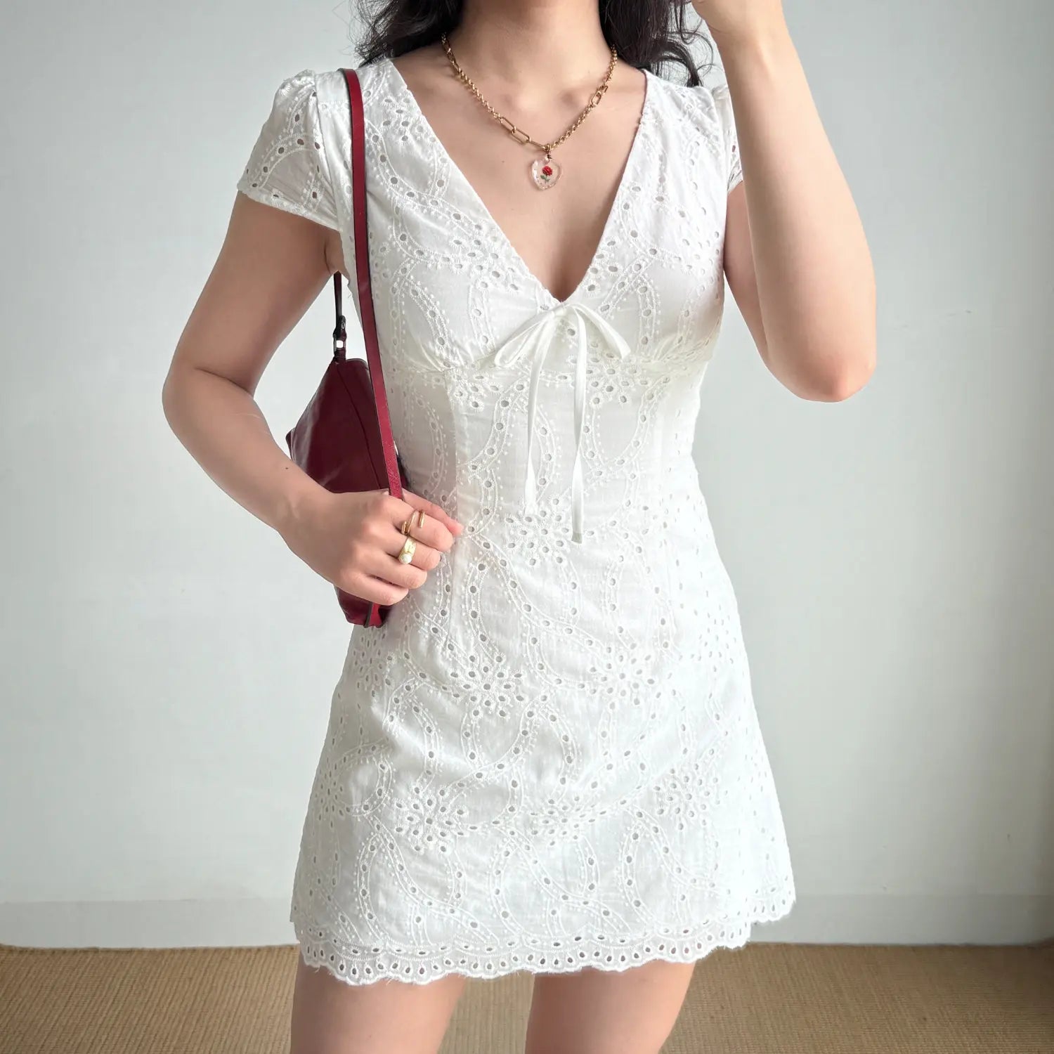  Lifestyle shot of a woman in a white eyelet embroidered mini dress, with one hand on her hip
