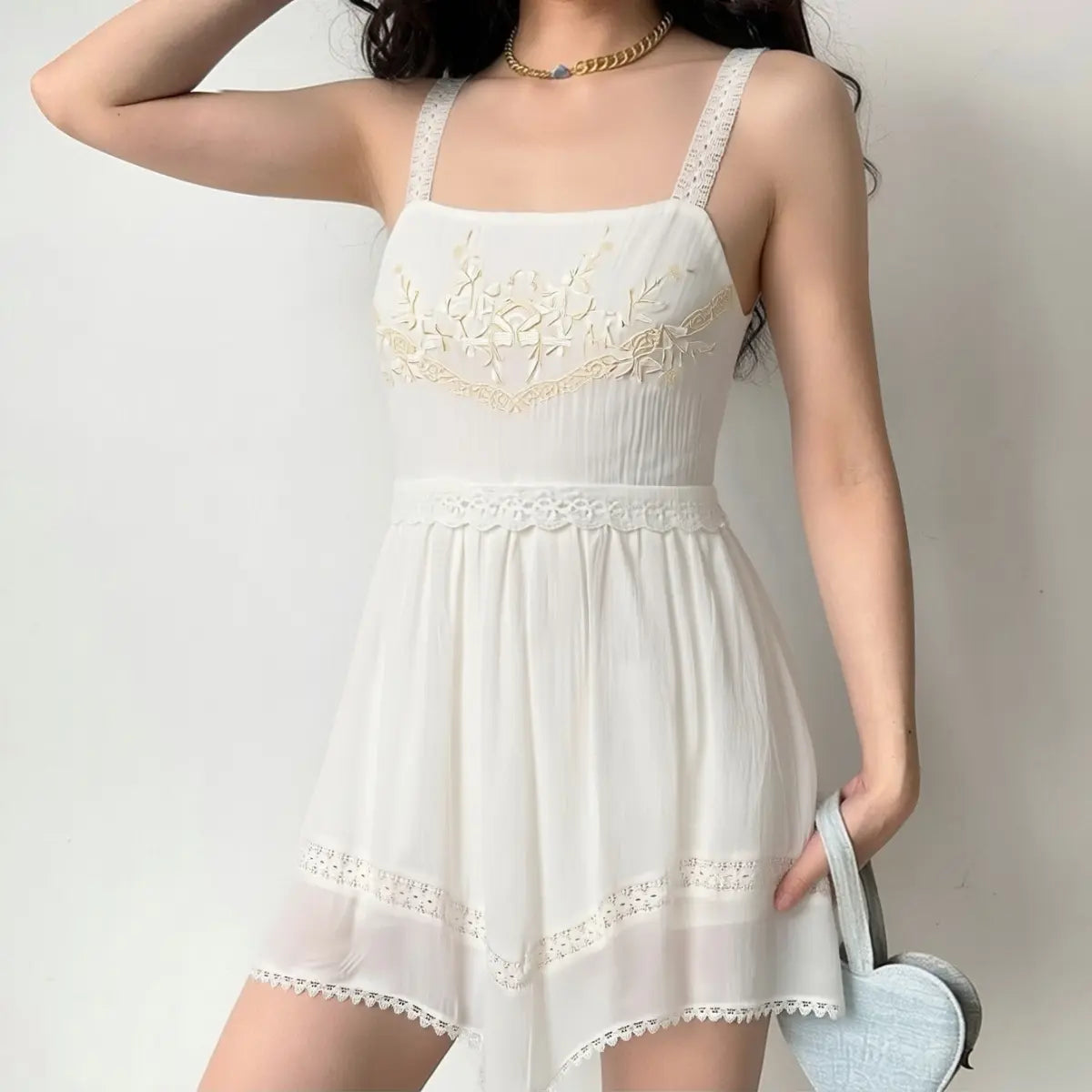 Model wearing white embroidered lace strap dress, styled with a light blue bag for a feminine casual look.