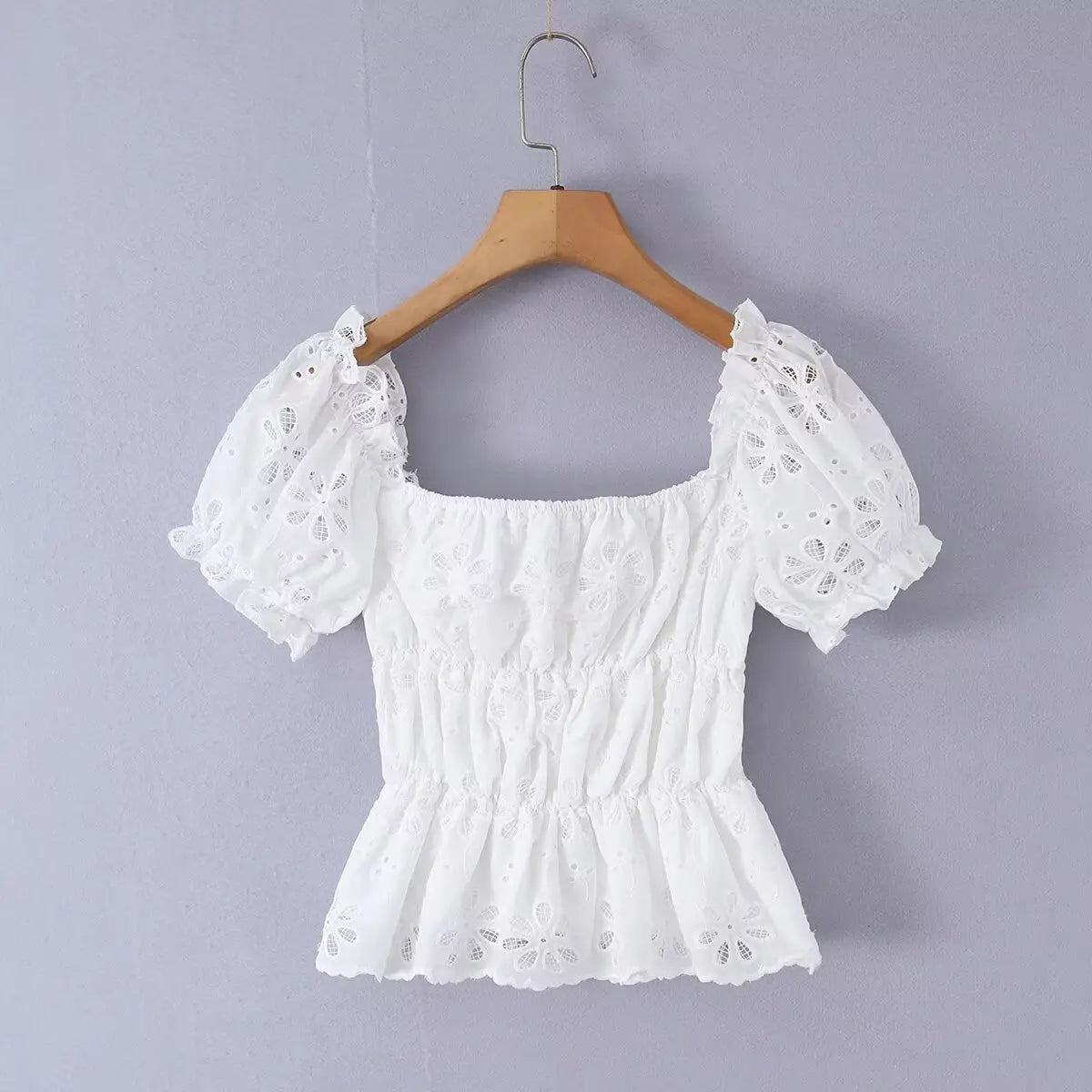 White eyelet embroidered top hanging on wooden hanger, full back view