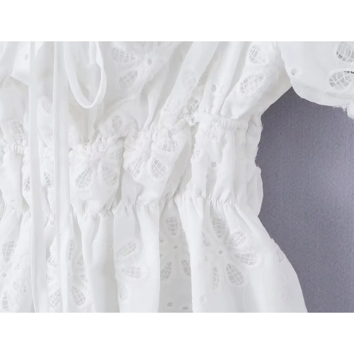 Close-up of the smocked waist, front tie detail, and eyelet embroidery on the white top