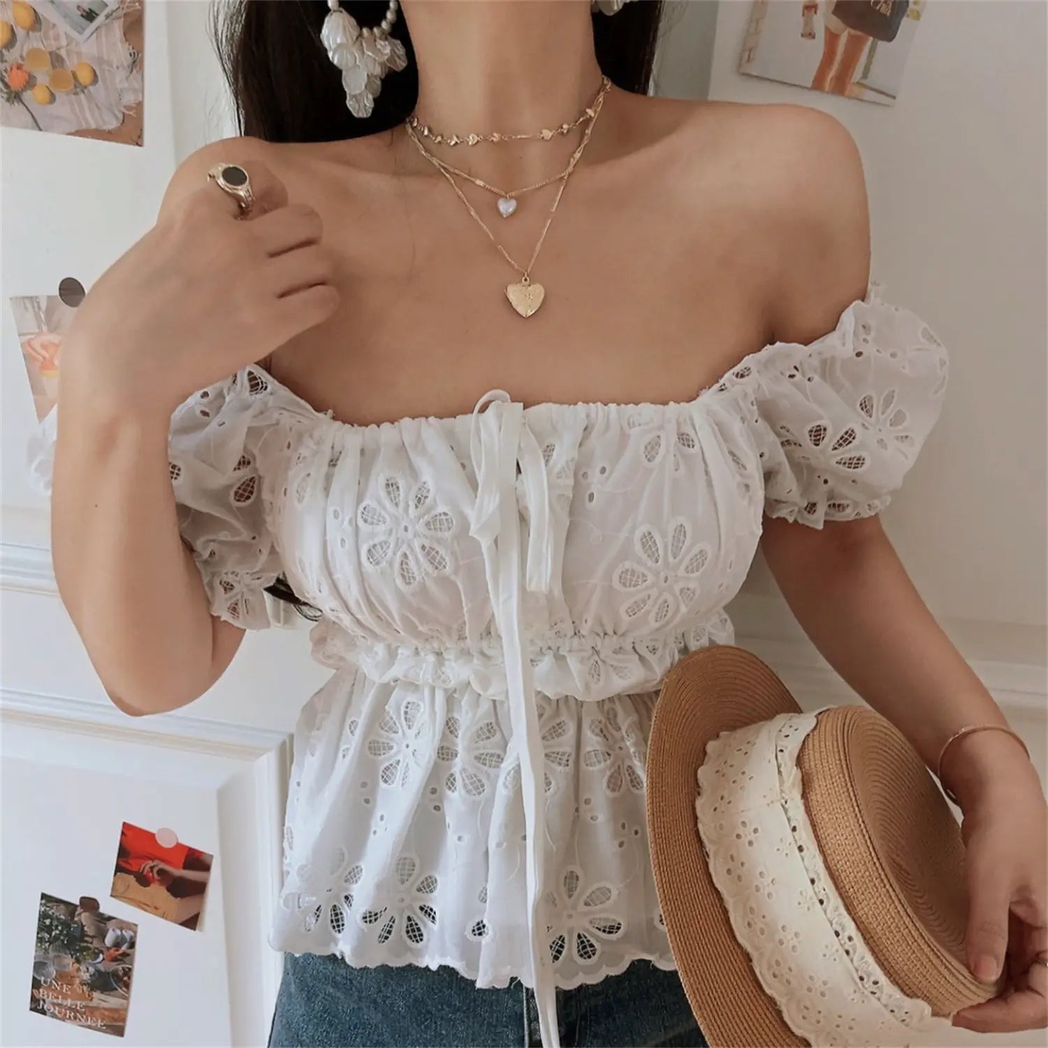 Lifestyle shot of model in the white embroidered off-shoulder peplum top, holding a straw bag