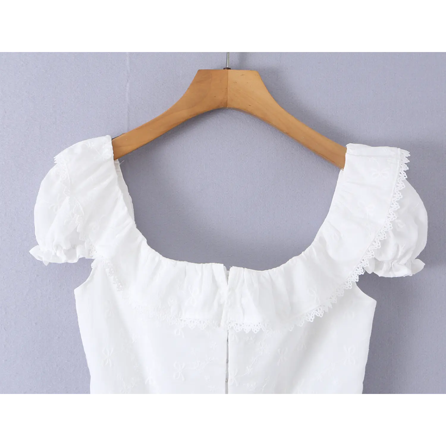 Close-up of the lace-trimmed square neckline and puff sleeve details on the white embroidered camisole