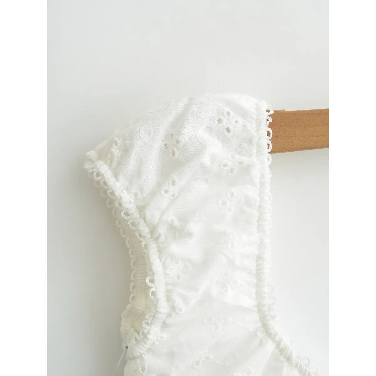 Close-up view of white square-neck top, showing eyelet embroidery, lace trim and gathered fabric details.