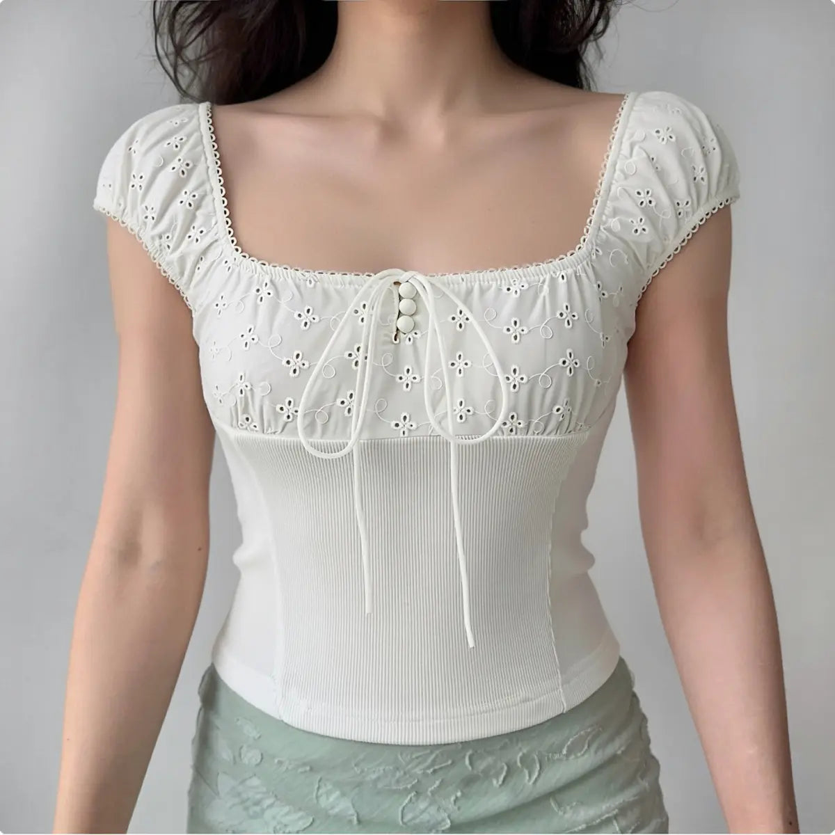 Model wearing white eyelet embroidered square neck top with ribbed bodice, styled with green skirt for casual everyday look.