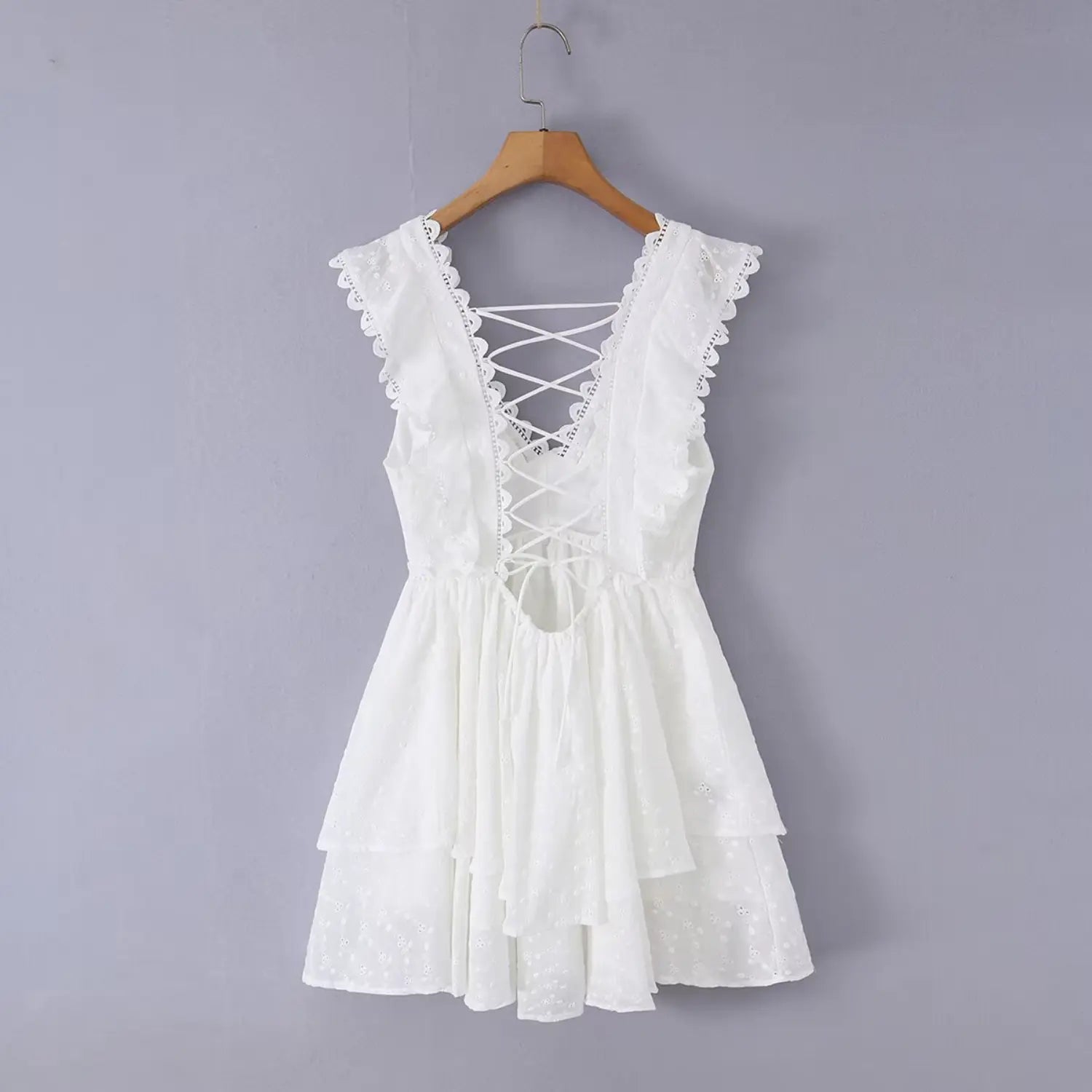Back view of the white eyelet dress hanging on a wooden hanger, highlighting the crisscross lace-up back